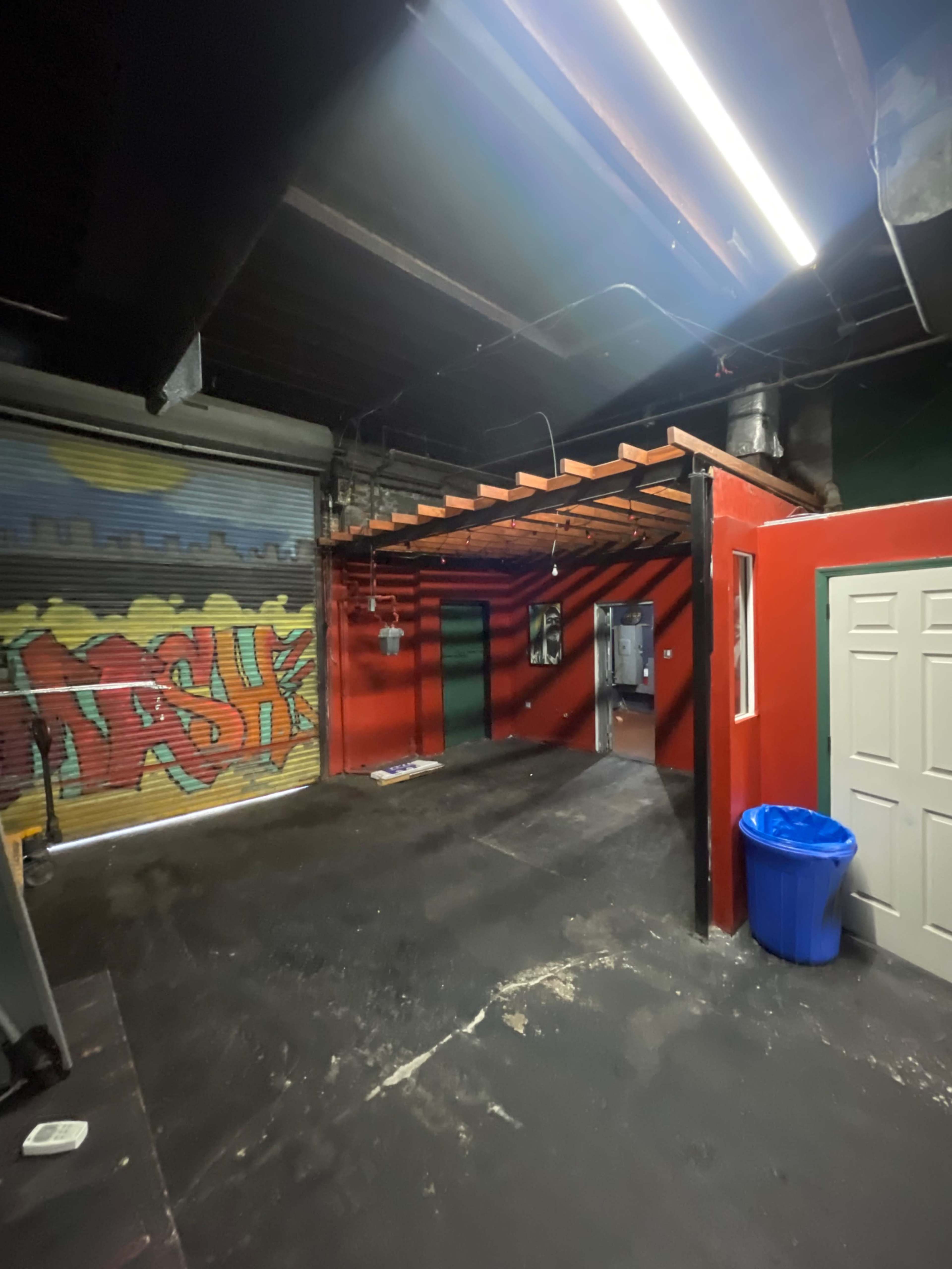 The image shows an industrial-style interior space with colorful graffiti on one wall, a red-painted wall, and a concrete floor.