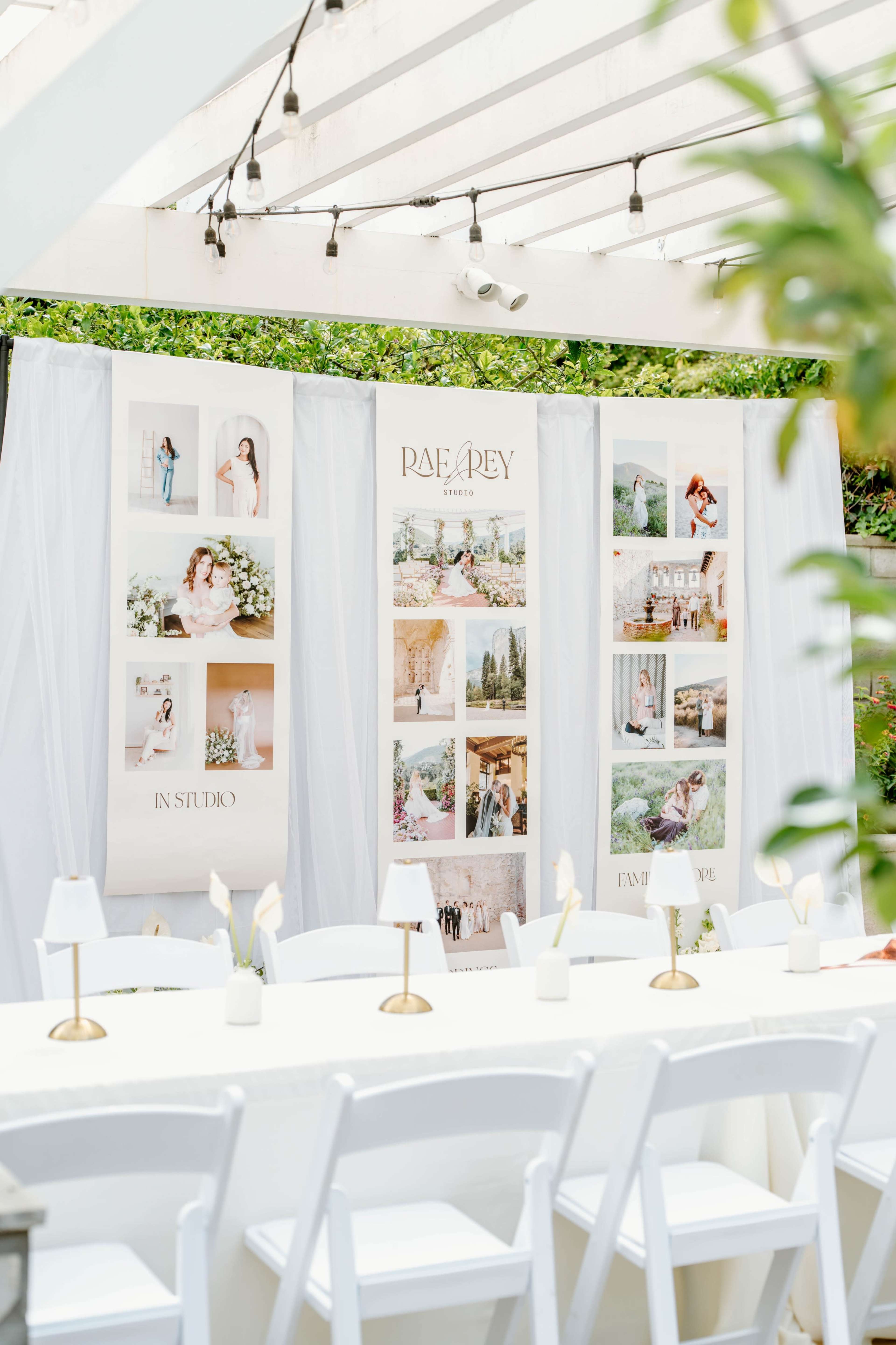 The image shows a decorated outdoor event space with white tables, elegant lighting, and display panels featuring photography.