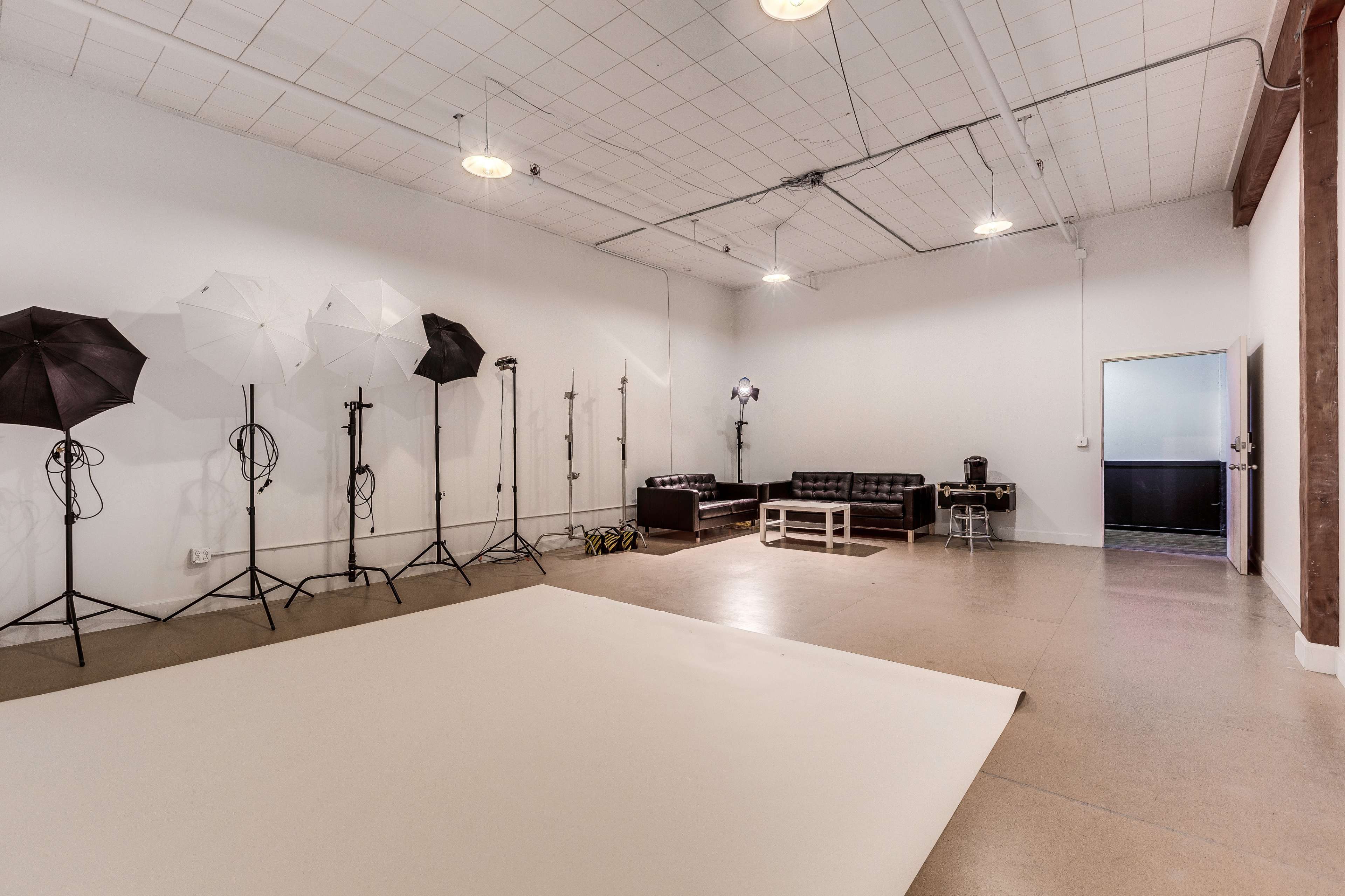 A spacious photography studio with various lighting equipment, a large backdrop, and seating arrangements.