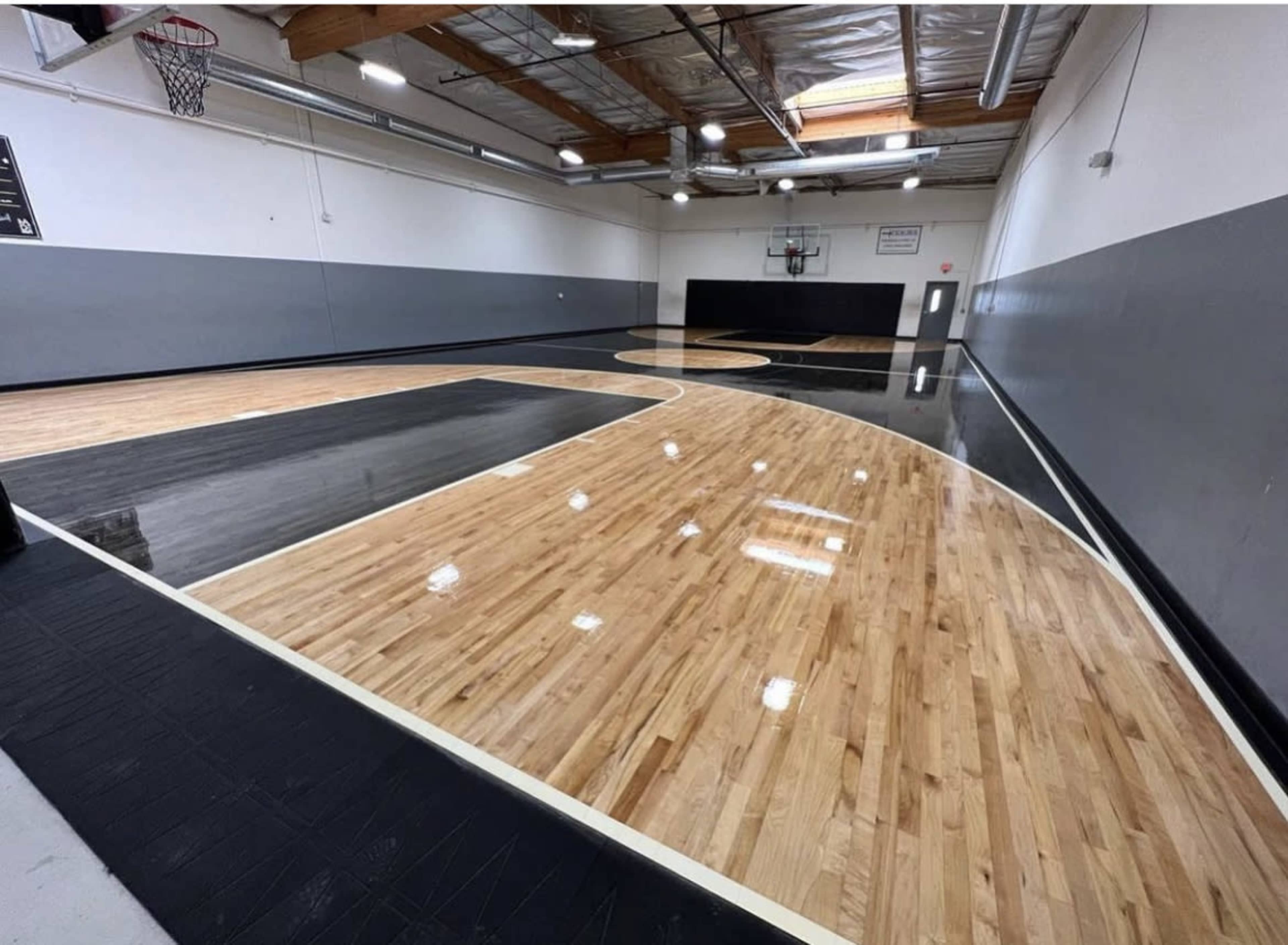 A polished indoor basketball court with black and wood laminate flooring under bright overhead lights.
