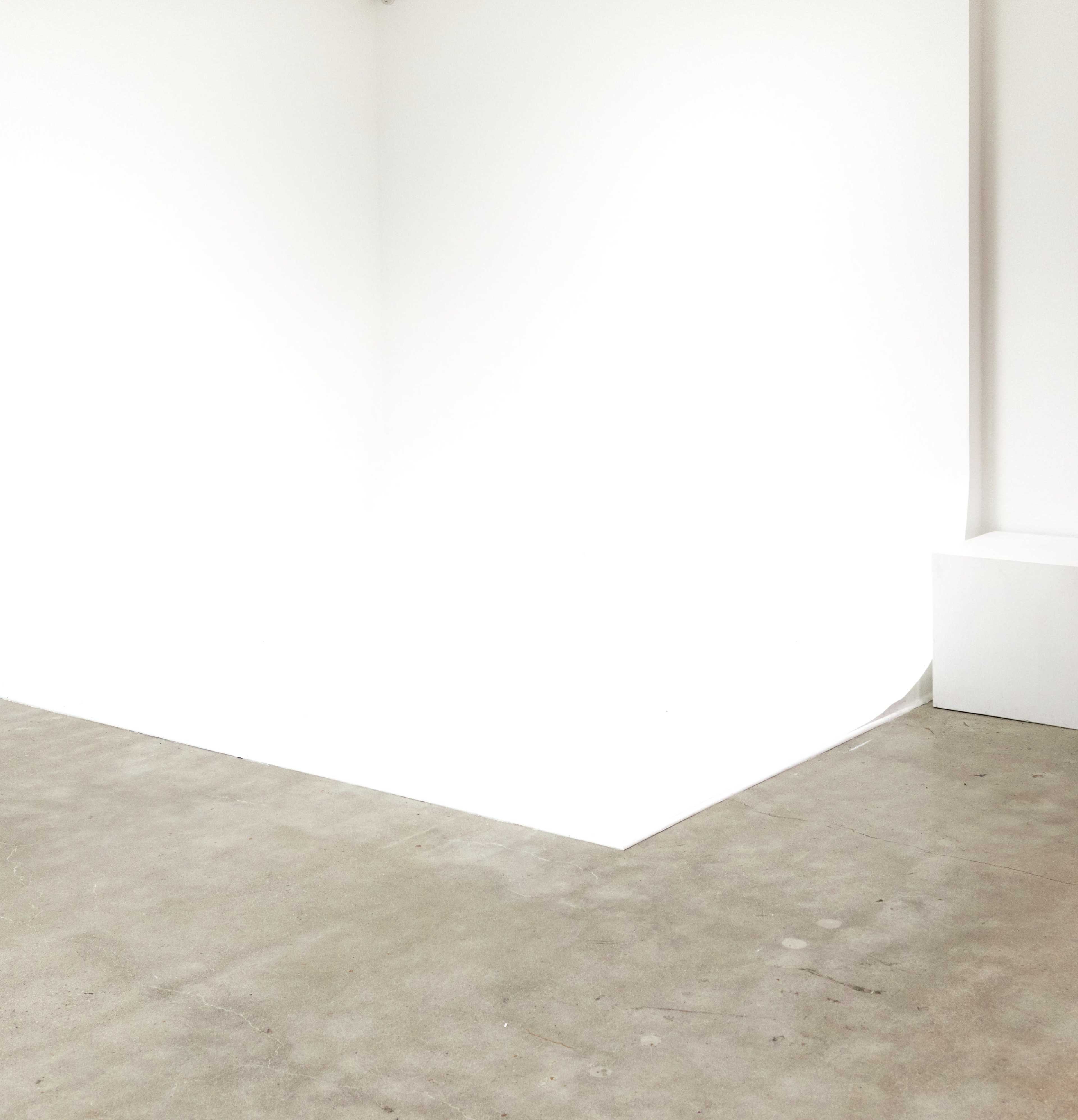 A stark white room with a concrete floor and a corner feature.