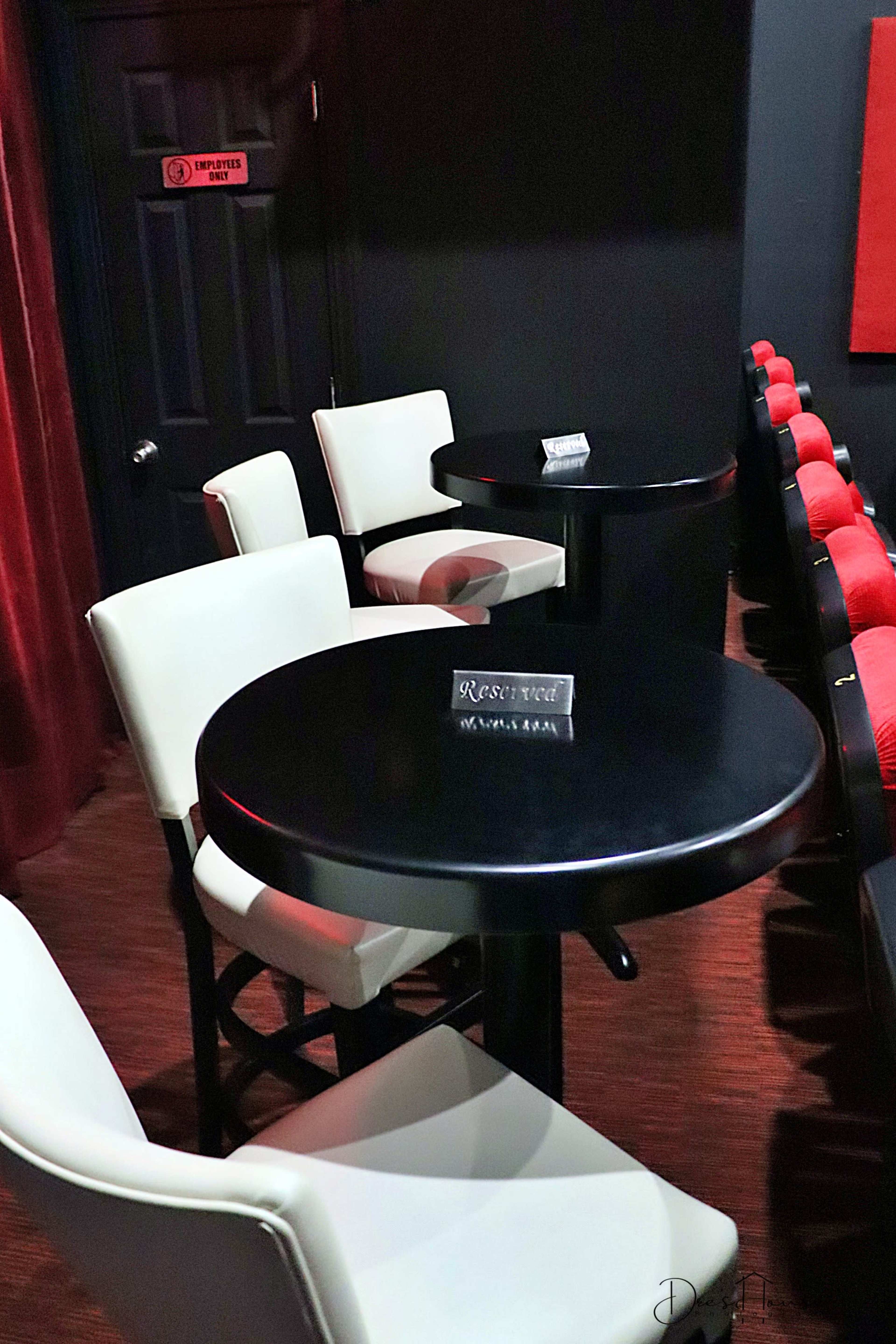 A dimly lit seating area with black tables and white chairs, featuring a "Reserved" sign on one table.