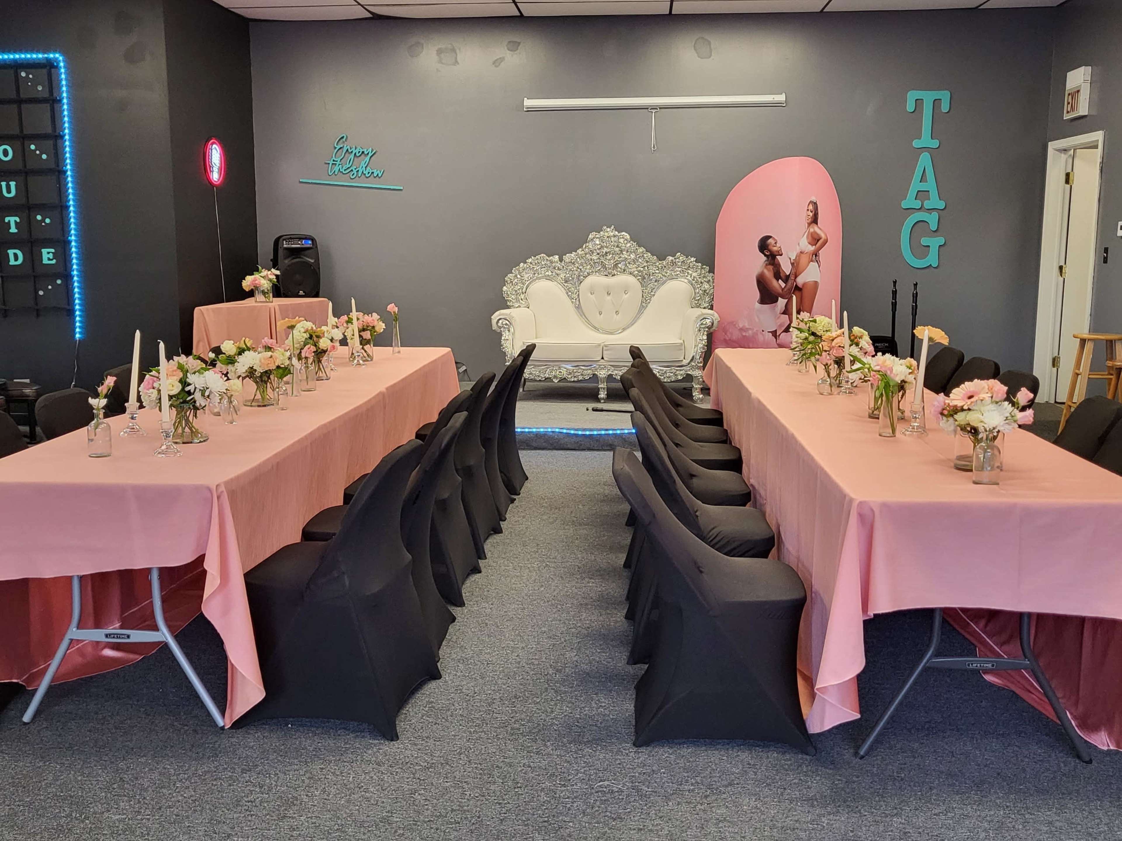 A decorated event space with two rows of tables dressed in pink and black, each adorned with floral centerpieces.