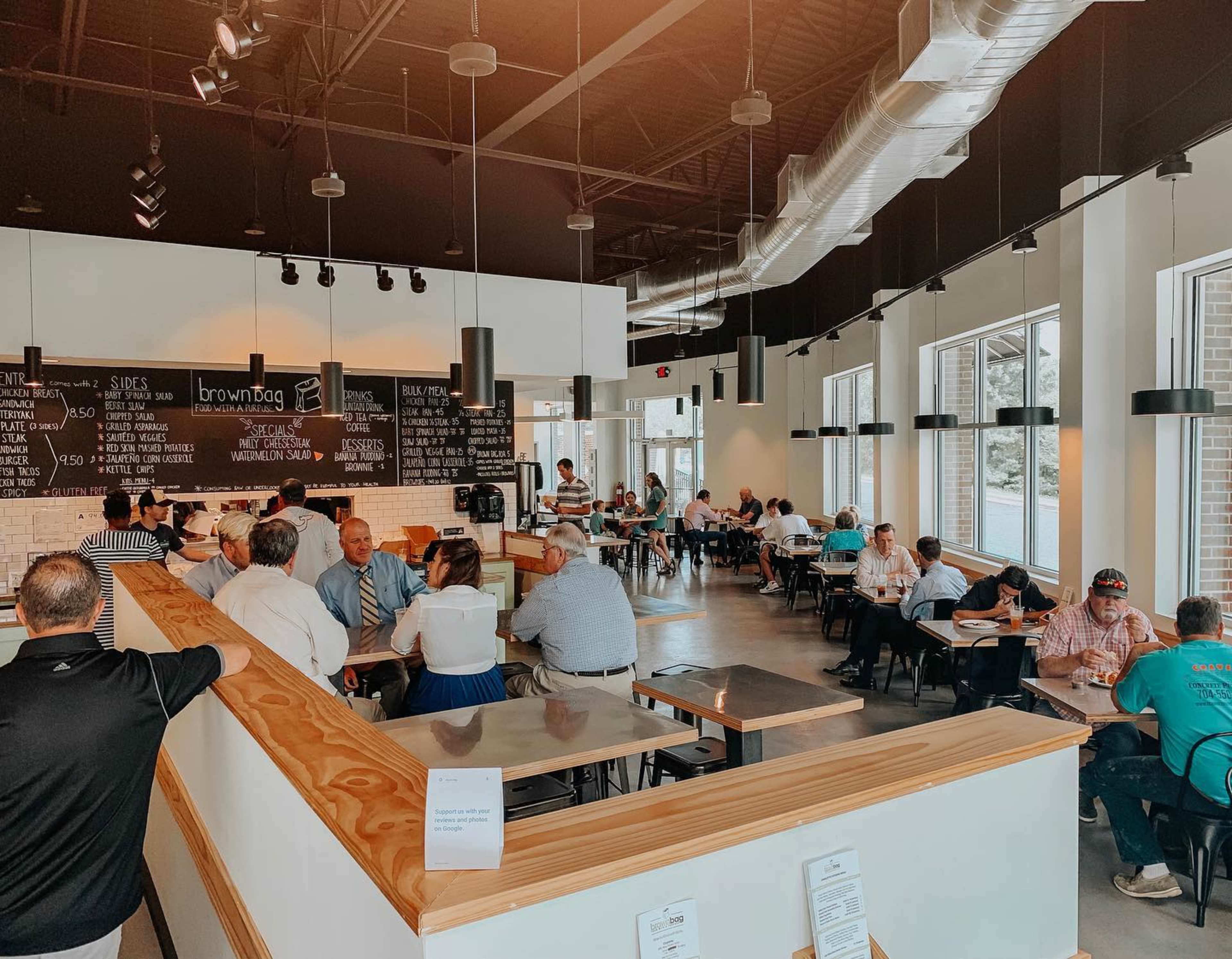 A spacious restaurant with a bustling atmosphere features patrons seated at tables and a large menu board on the wall.