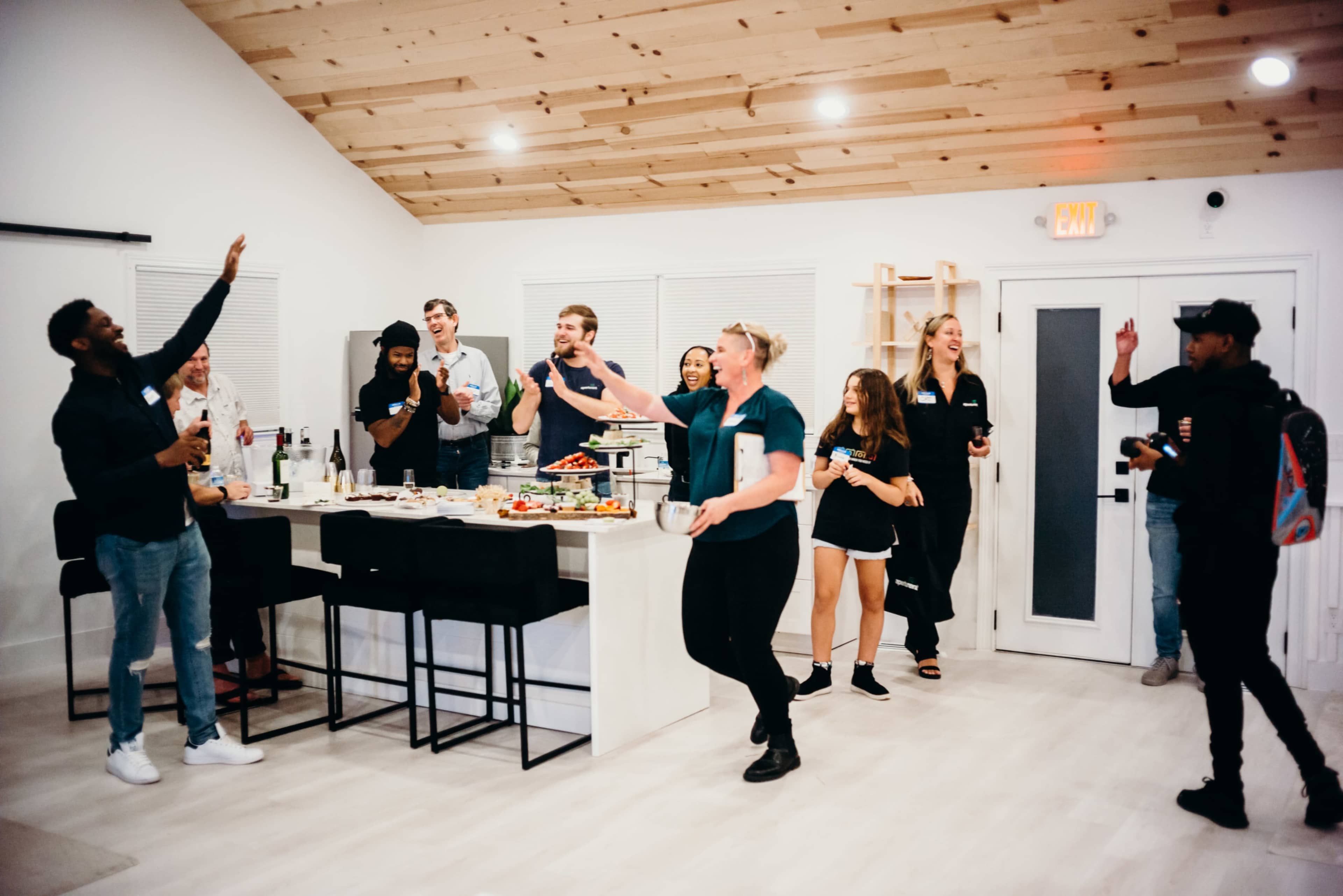 A diverse group of people socialize in a modern kitchen-living space while enjoying food and drinks.