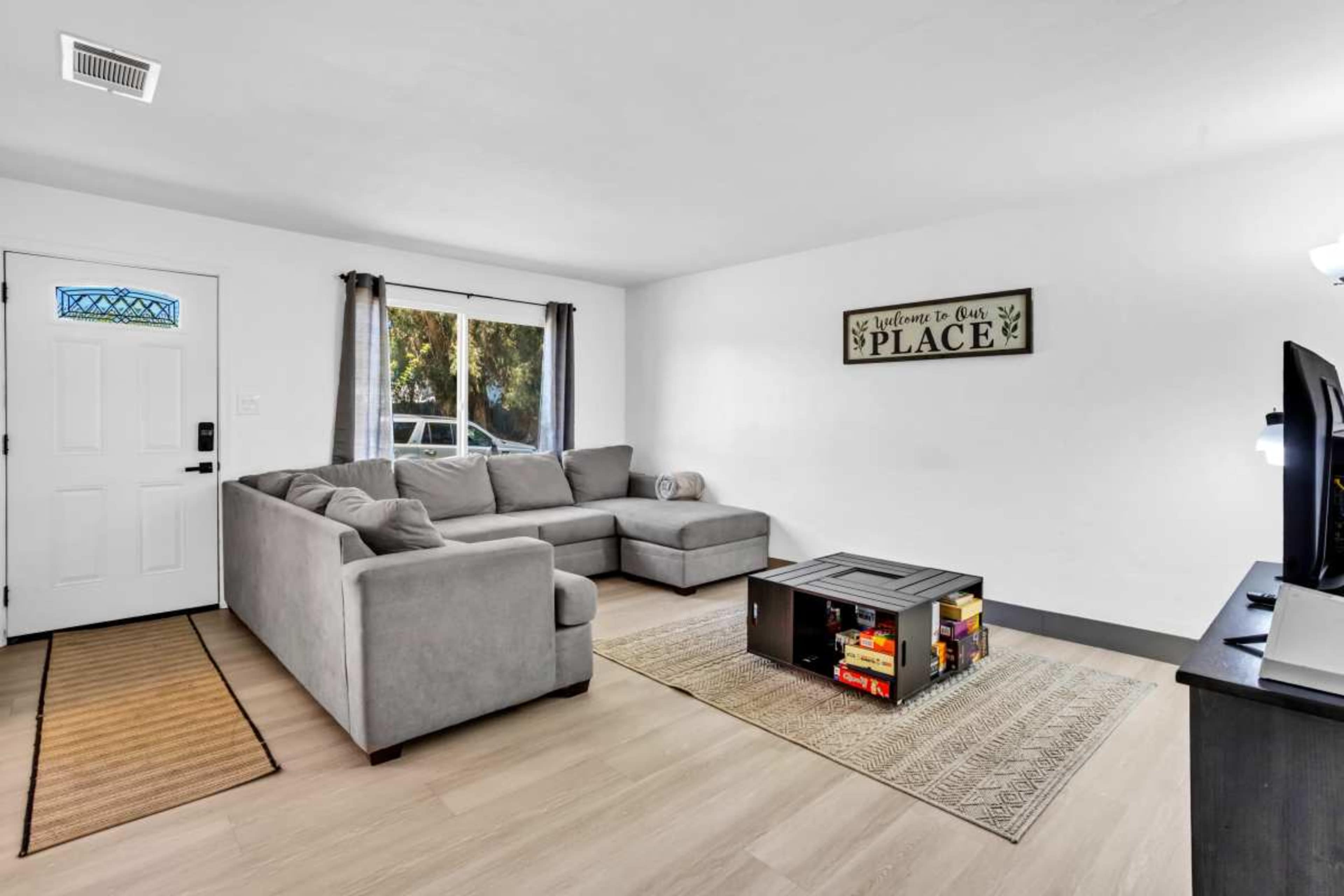 A modern living room features a gray sectional sofa, a coffee table made of crates, and a decorative sign on the wall.