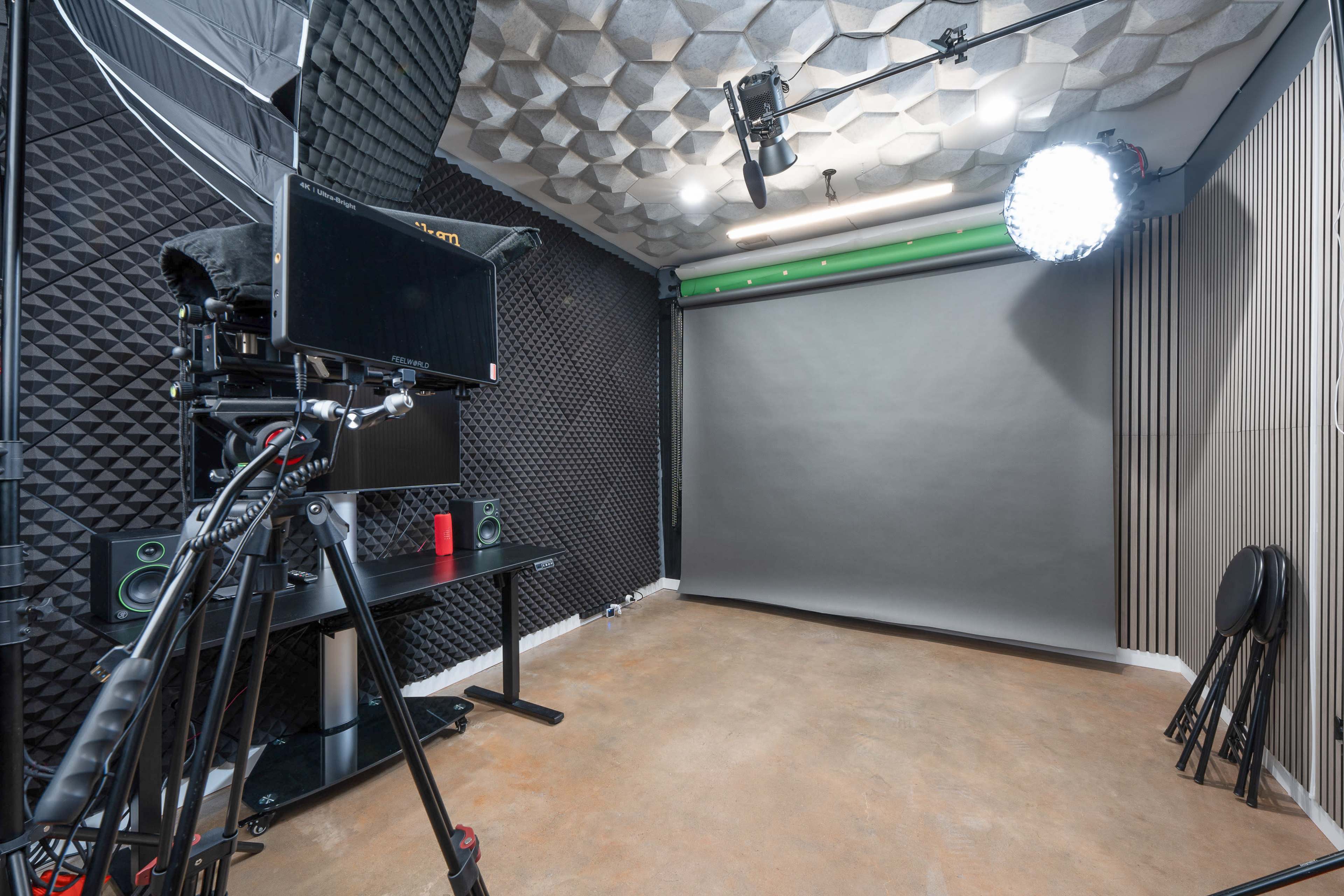 The image shows a photography studio equipped with a camera on a tripod, lighting fixtures, a green backdrop, and black acoustic paneling on the walls.