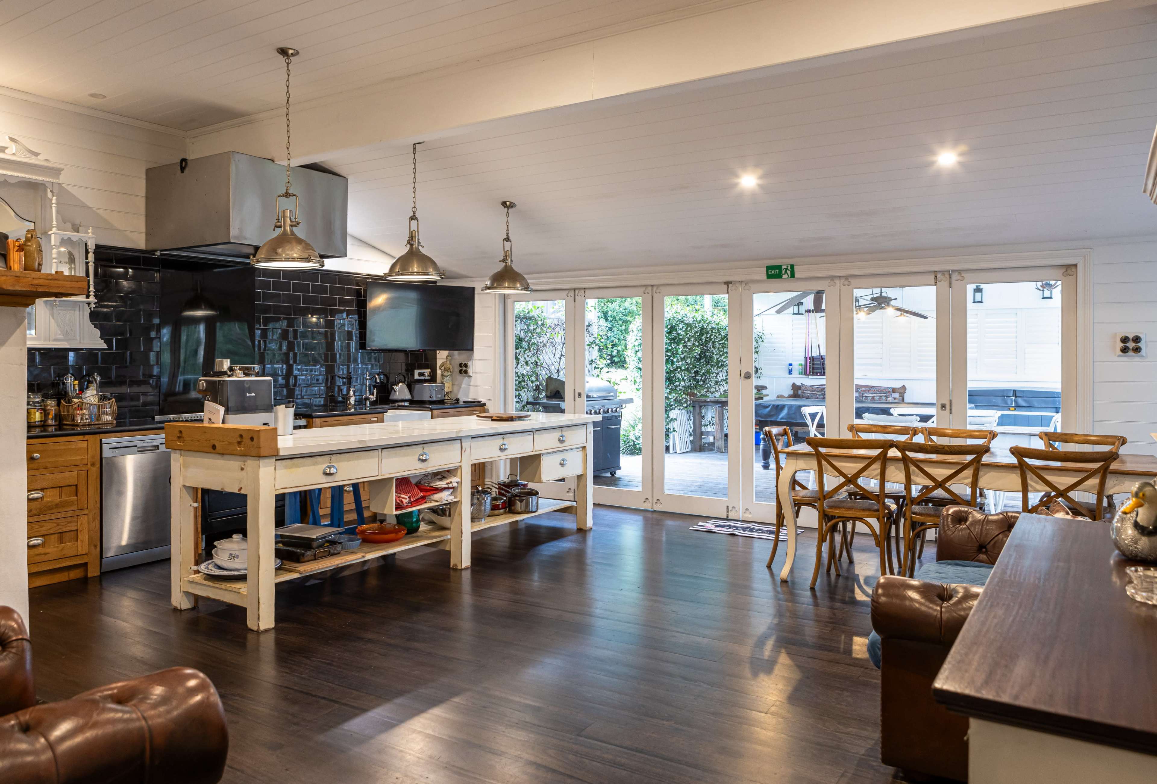 The image shows a spacious kitchen with a large central island, featuring wooden cabinetry, modern appliances, and an adjoining dining area with wooden chairs and a table.
