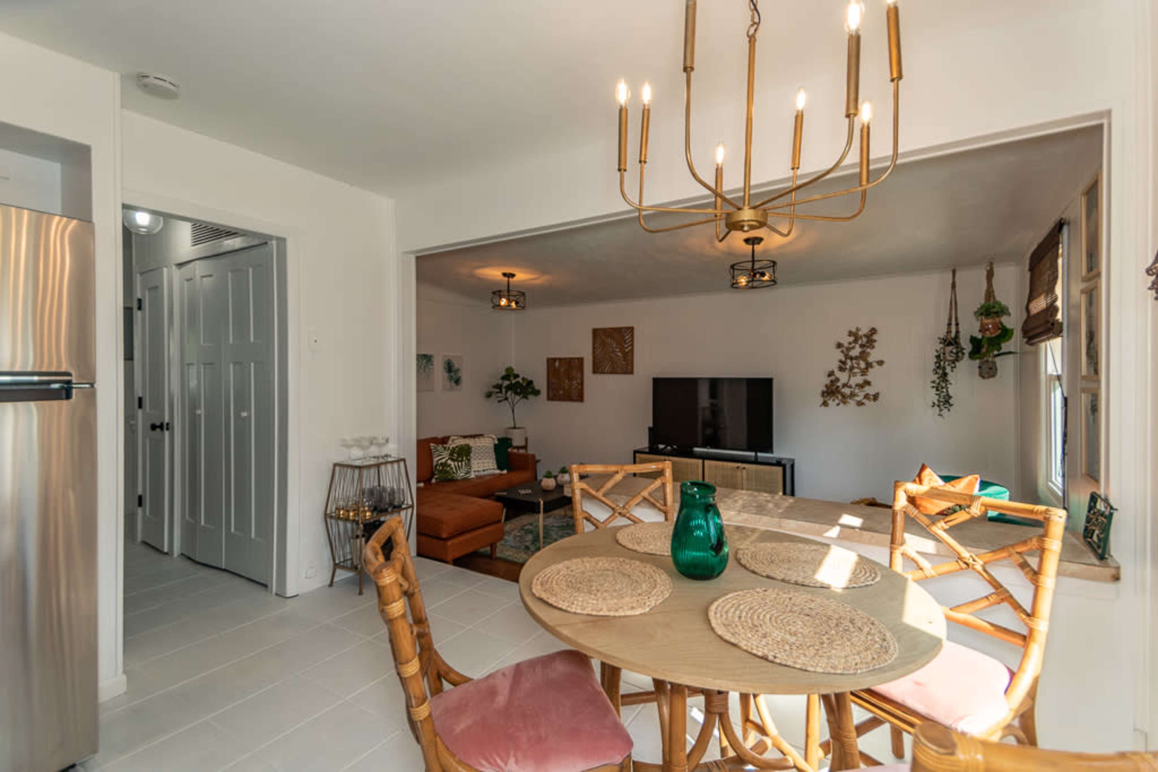 A dining area with a round table and four chairs is positioned near a living room featuring a television and a brown sofa.
