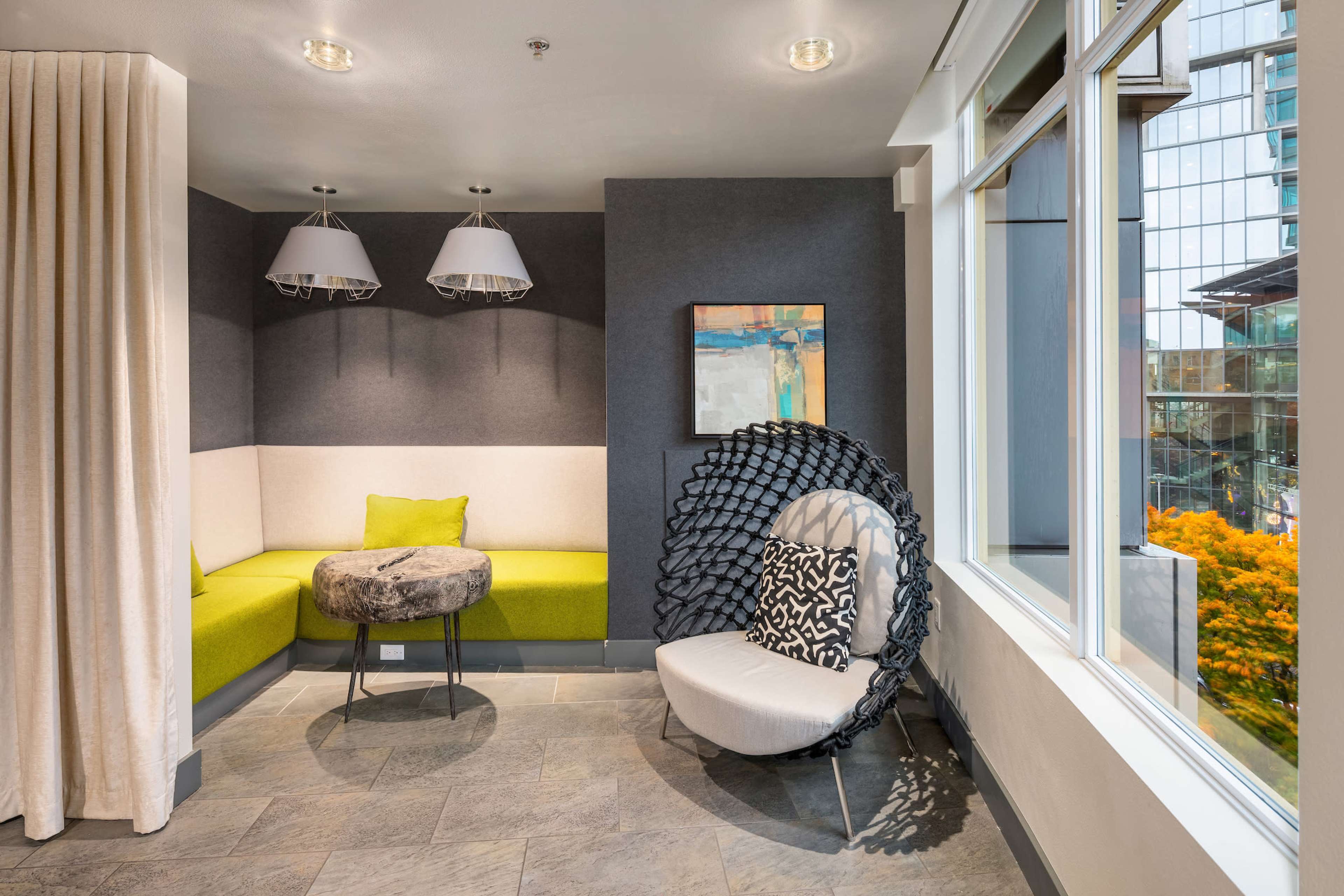 A modern seating area with a curved green bench, a small table, and a large decorative chair positioned near a window.