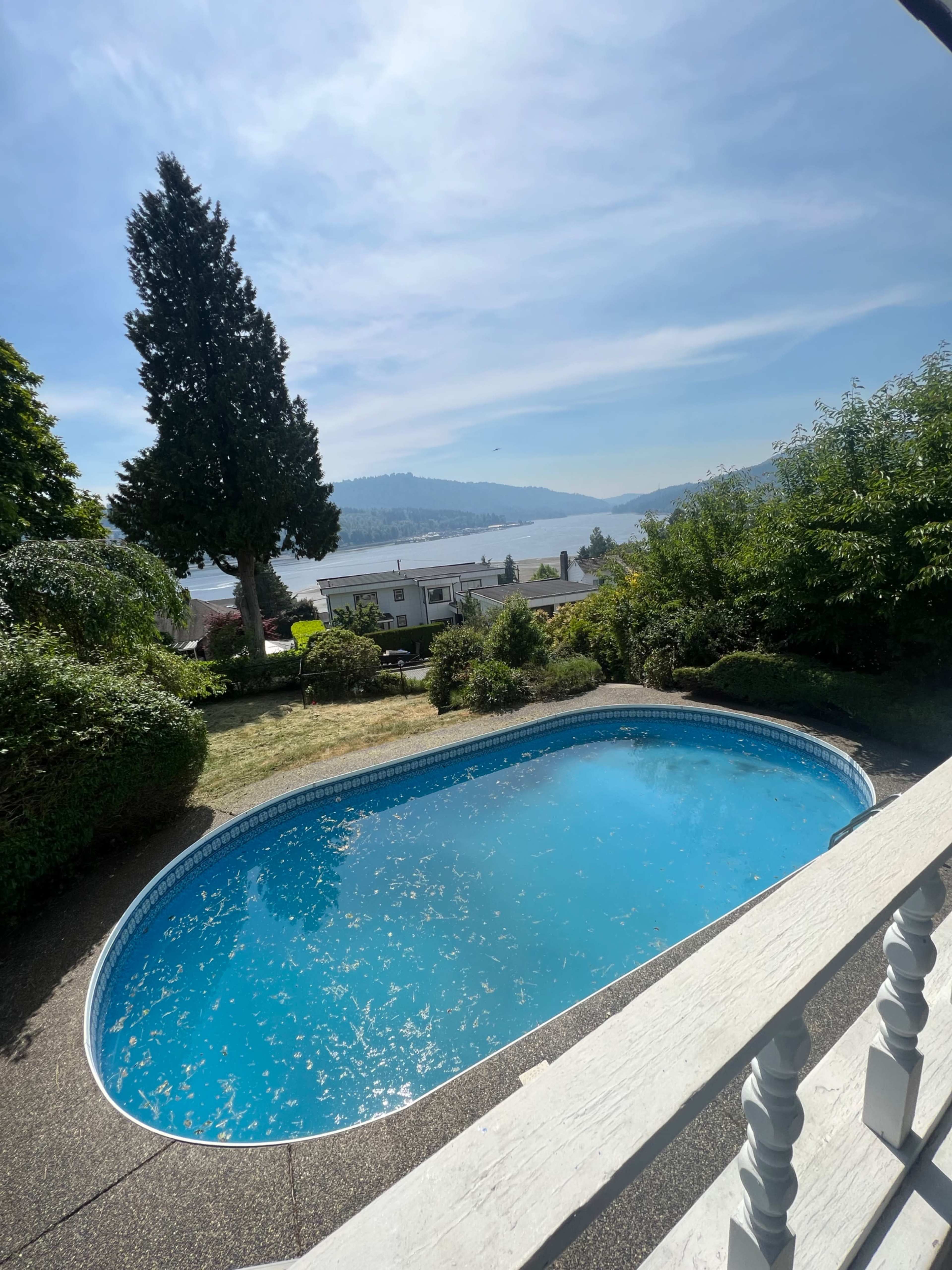 A blue swimming pool surrounded by greenery and a view of a lake and hills in the background.