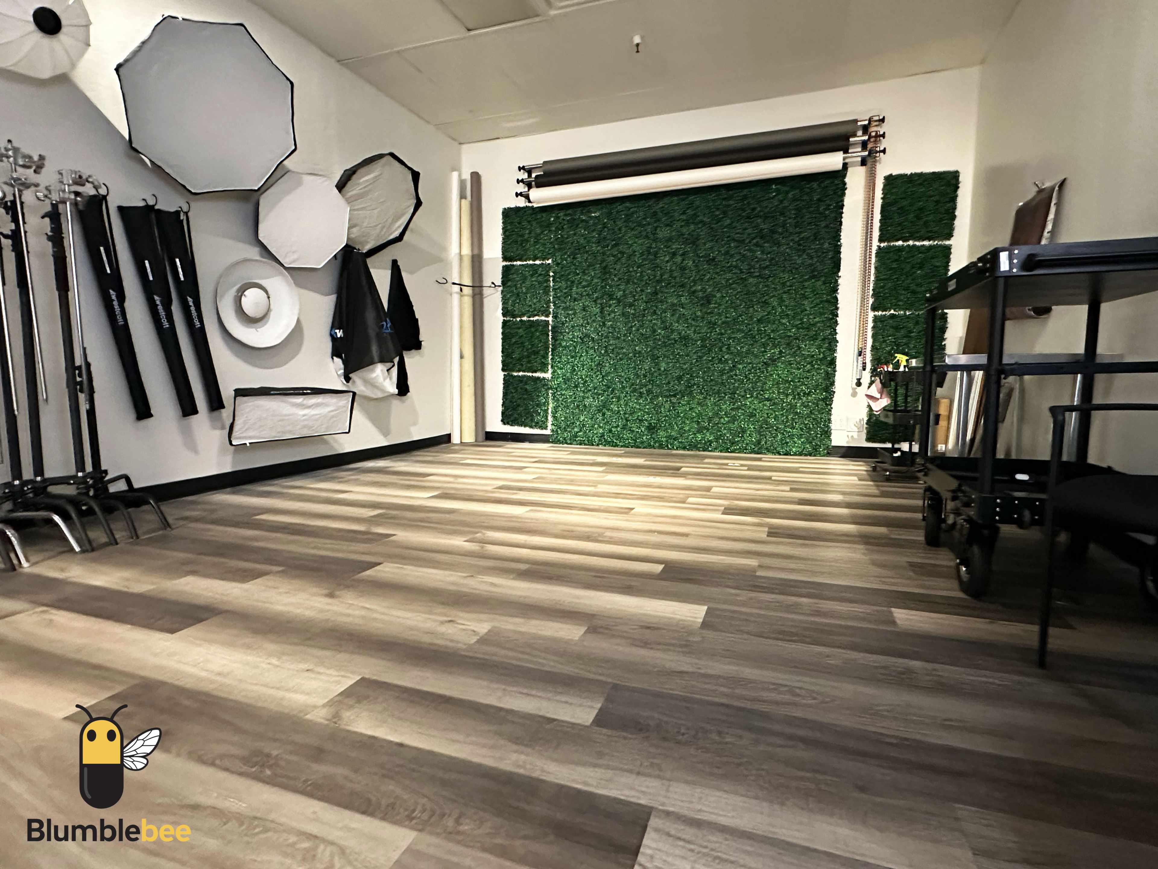 The image shows a photography studio with various lighting equipment mounted on the walls and a green backdrop on one side.