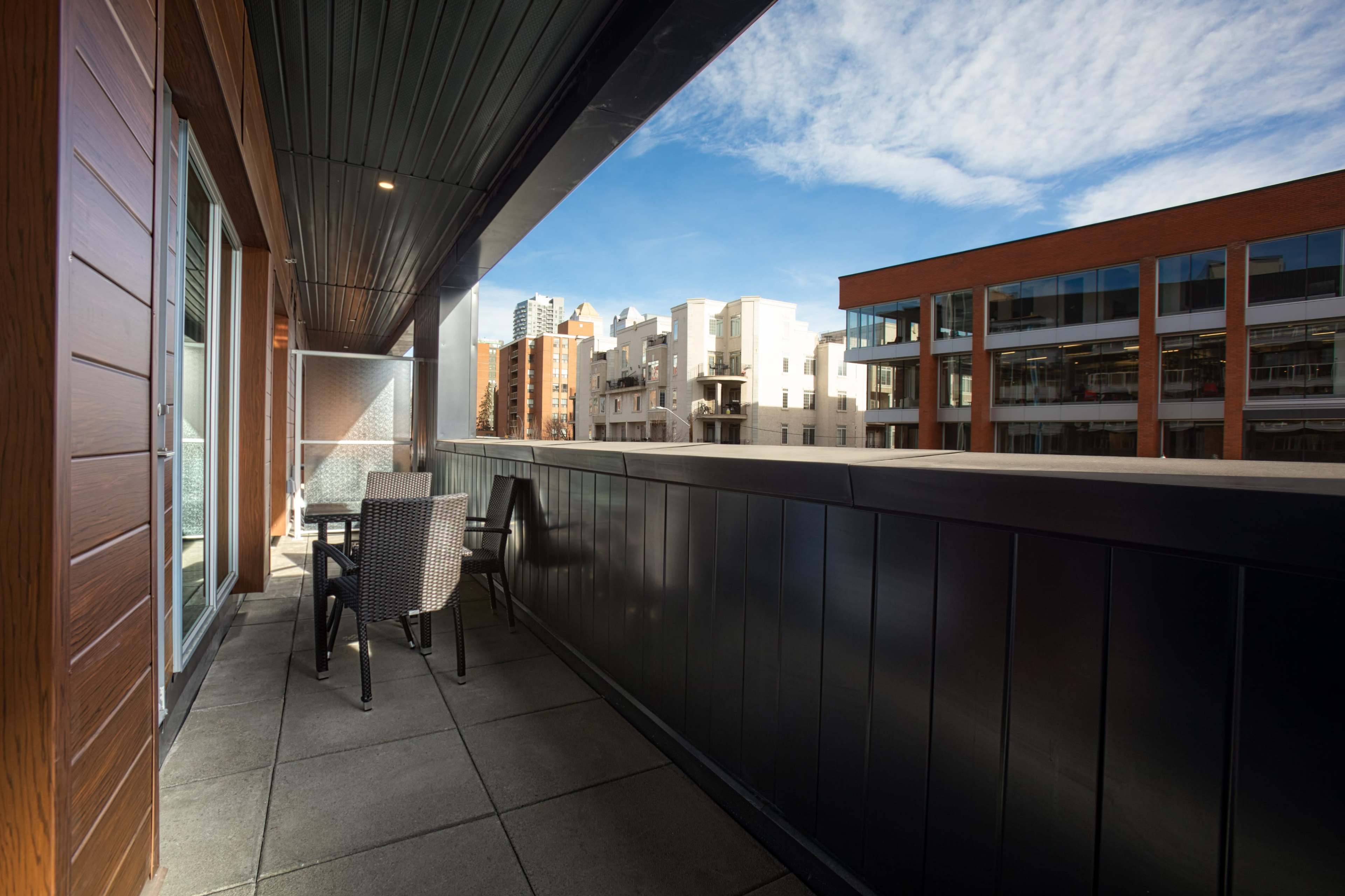 A balcony with a table and chairs overlooks a buildingscape under a bright sky.