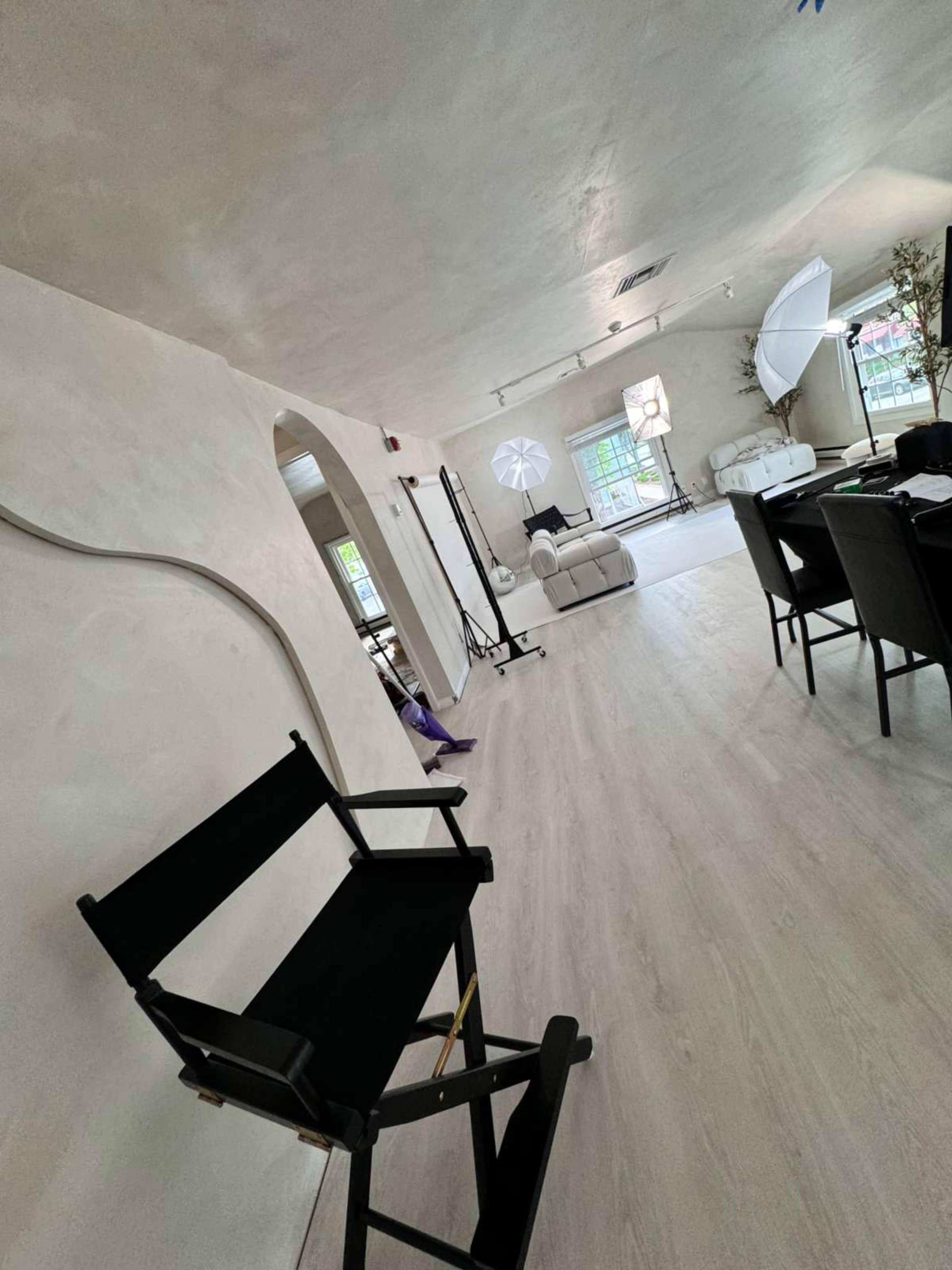 A well-lit studio or living space featuring a director's chair, a mirror, photography lights, and modern furniture.