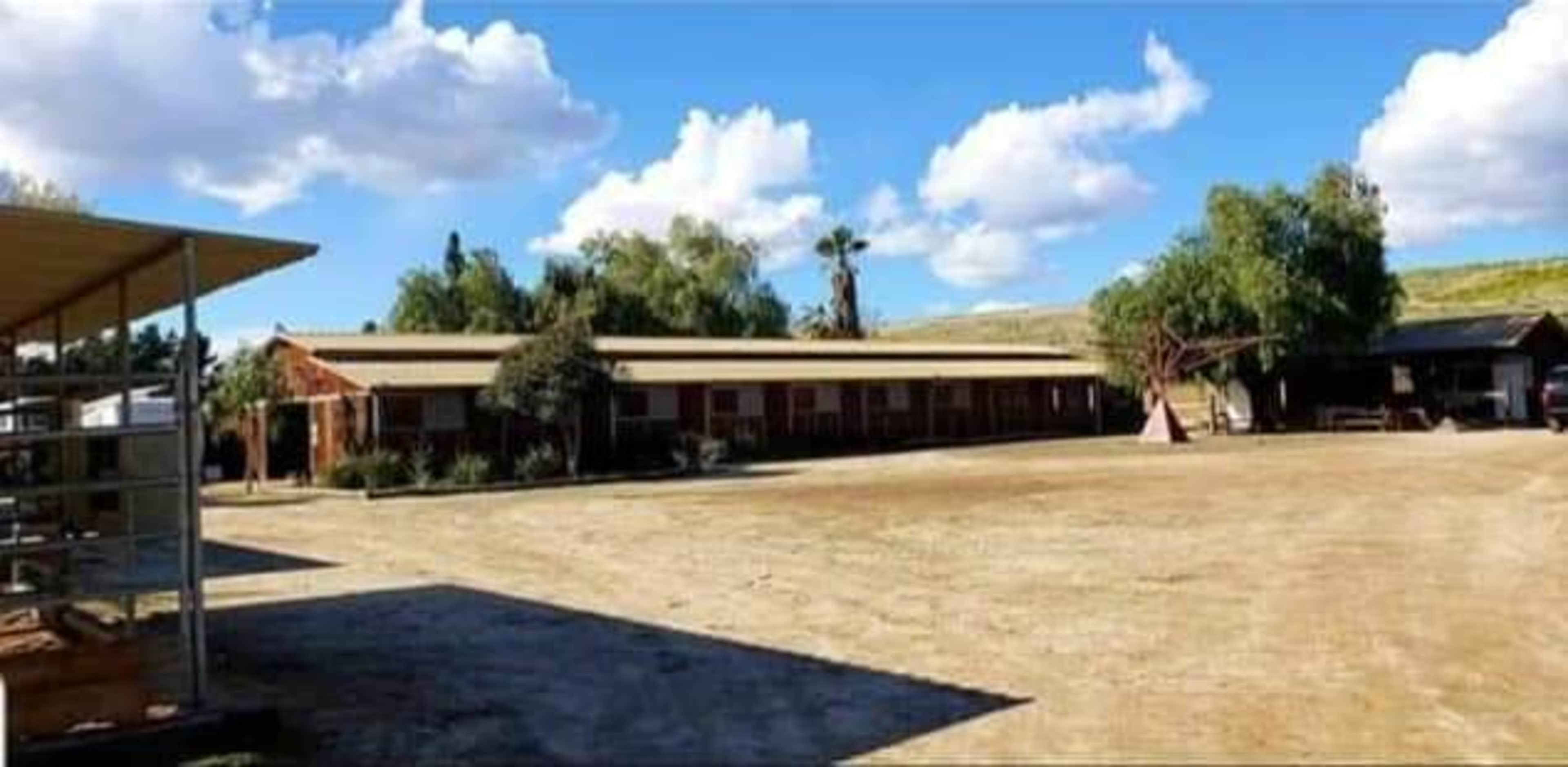 A row of buildings near a dirt area with a few trees and scattered clouds in the sky.