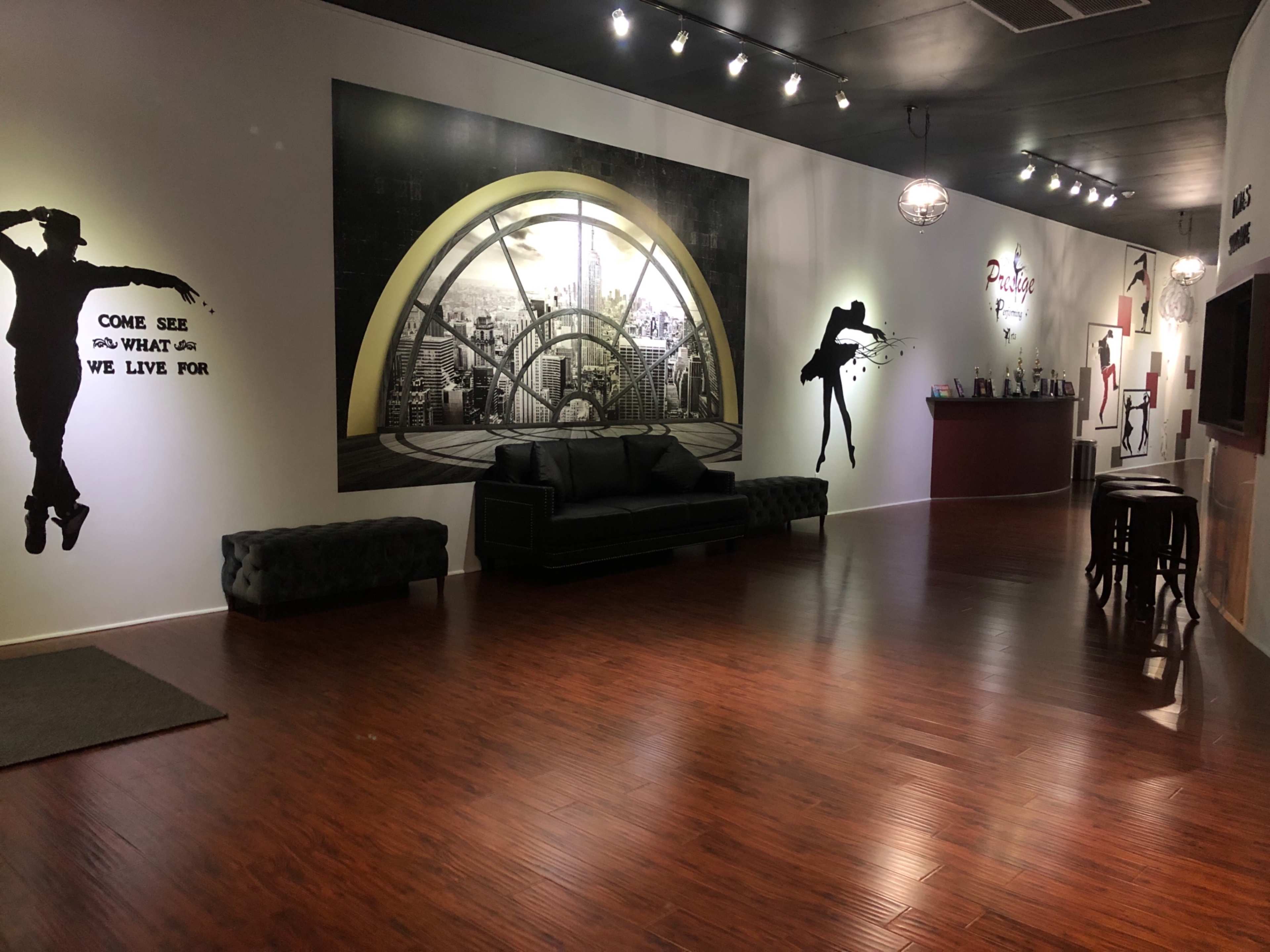 An interior space featuring a large mural of a cityscape, black and white silhouette artwork on the walls, a black sofa, and a bar area in the background.