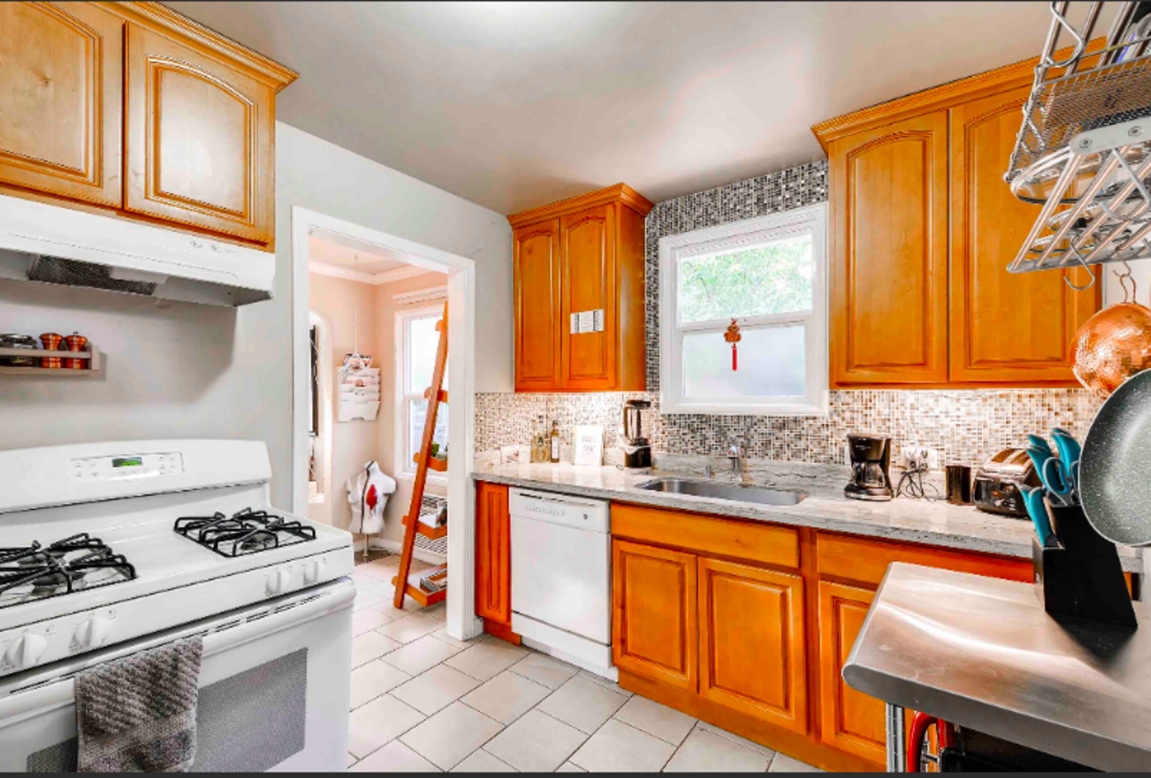 The kitchen features wooden cabinetry, a gas stove, a dishwasher, and a stainless steel countertop with mosaic tile backsplash.