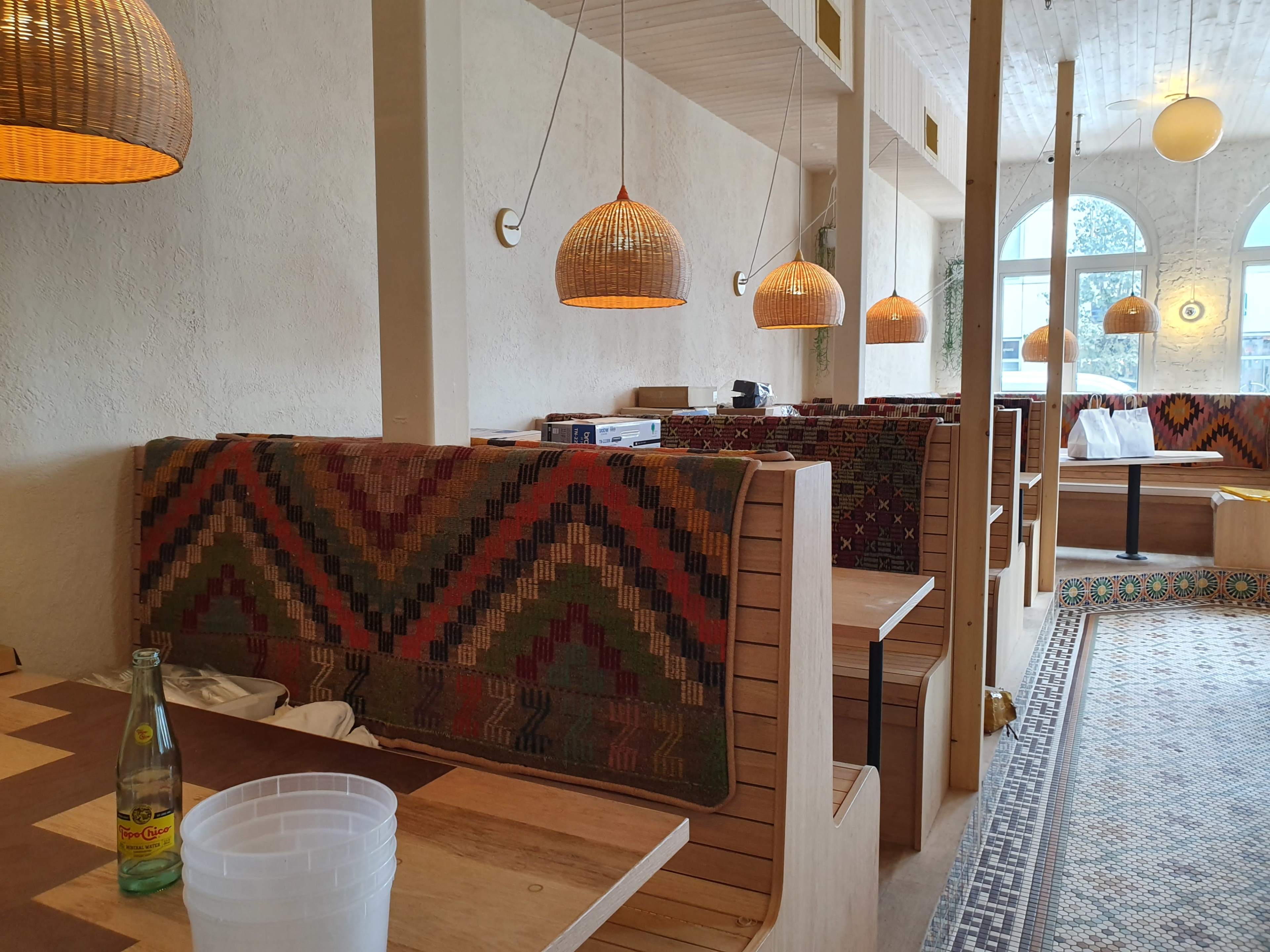 A modern restaurant interior with upholstered booths, pendant lighting, and a patterned floor.