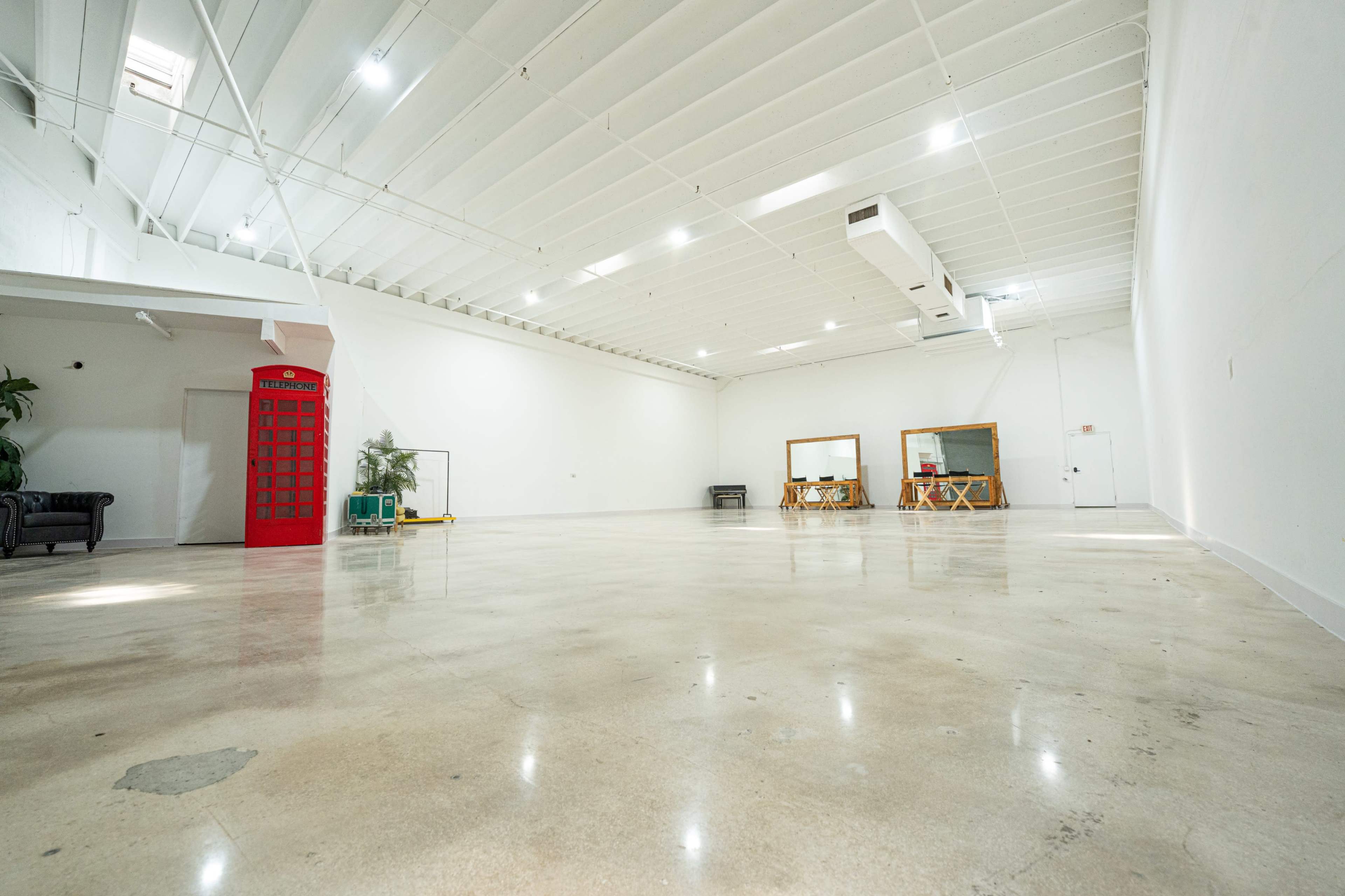 The image shows a spacious, empty room with polished concrete floors, a red telephone booth in one corner, and two large mirrors against the wall.