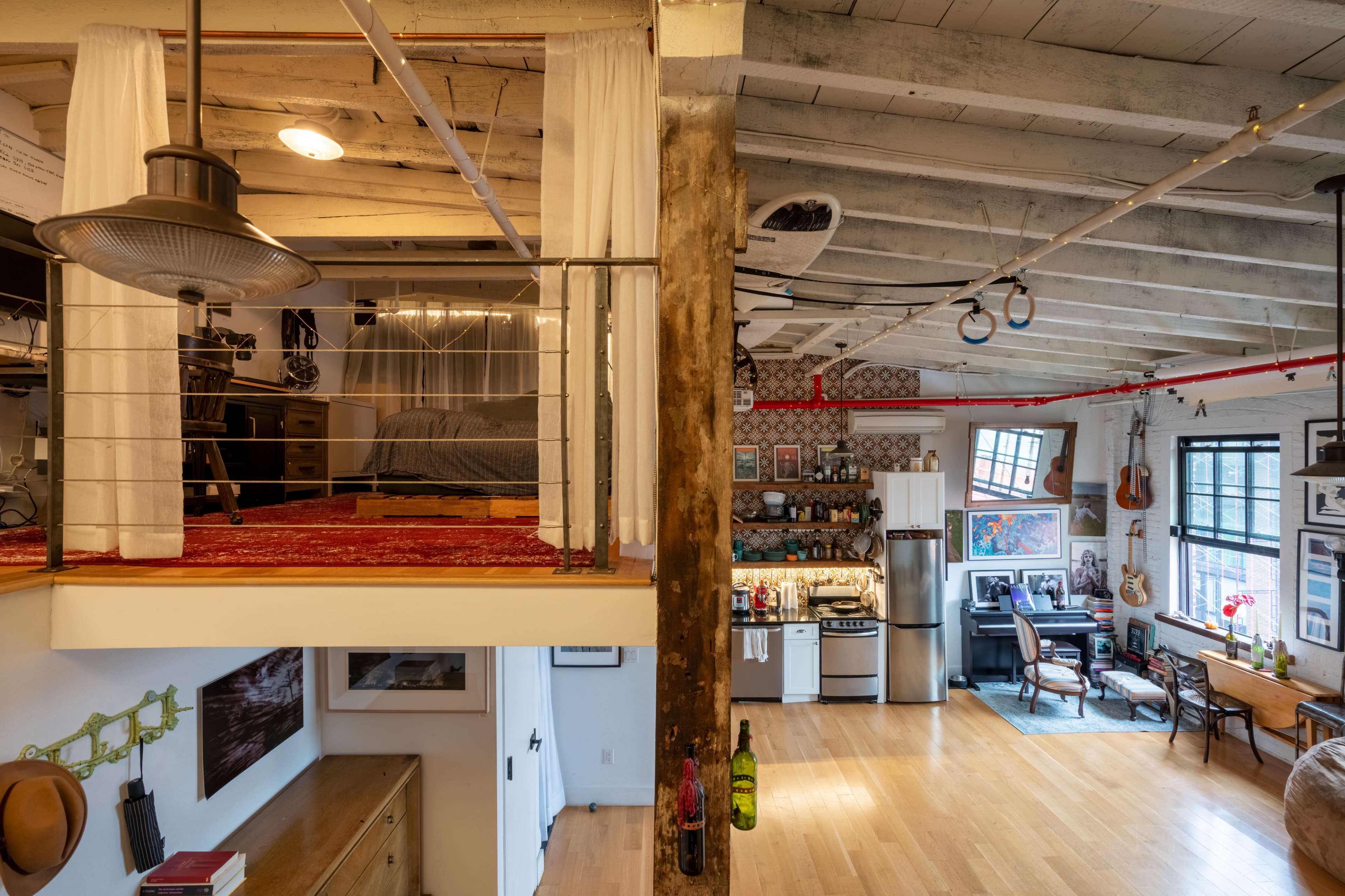 The image shows a spacious loft-style apartment featuring a mezzanine sleeping area and an open kitchen-living room layout with various artworks on the walls.