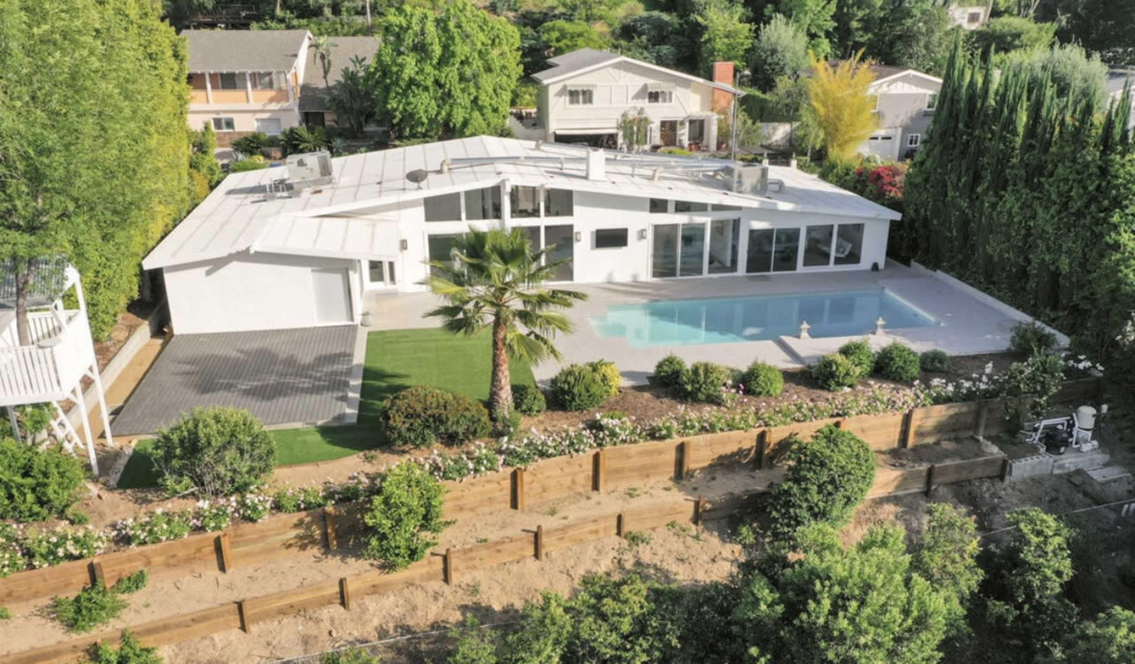 A modern single-story house with a swimming pool and surrounding landscaping, situated on a hillside.