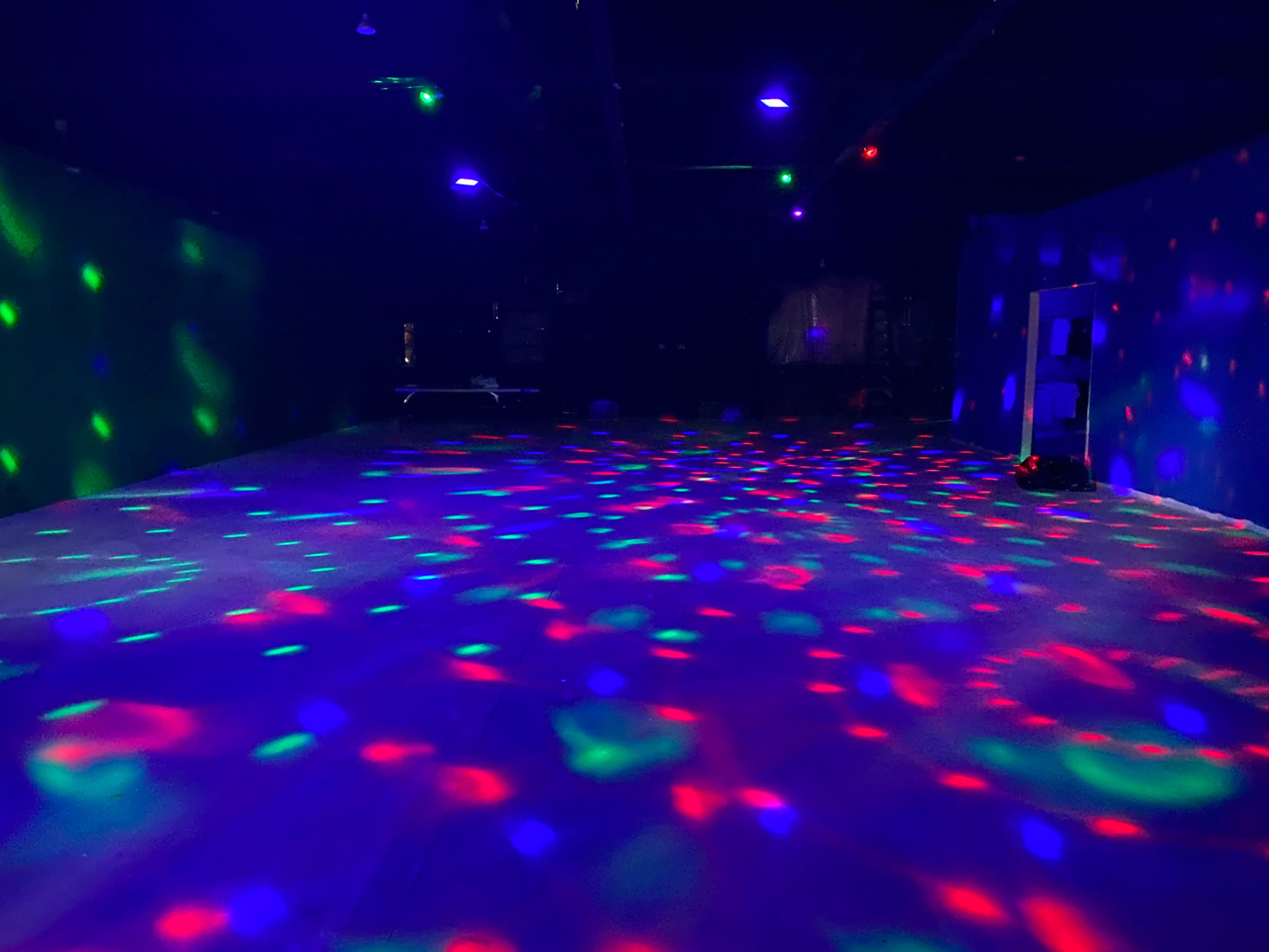 The image shows a dimly lit room with colorful lights creating patterns on the floor and walls.