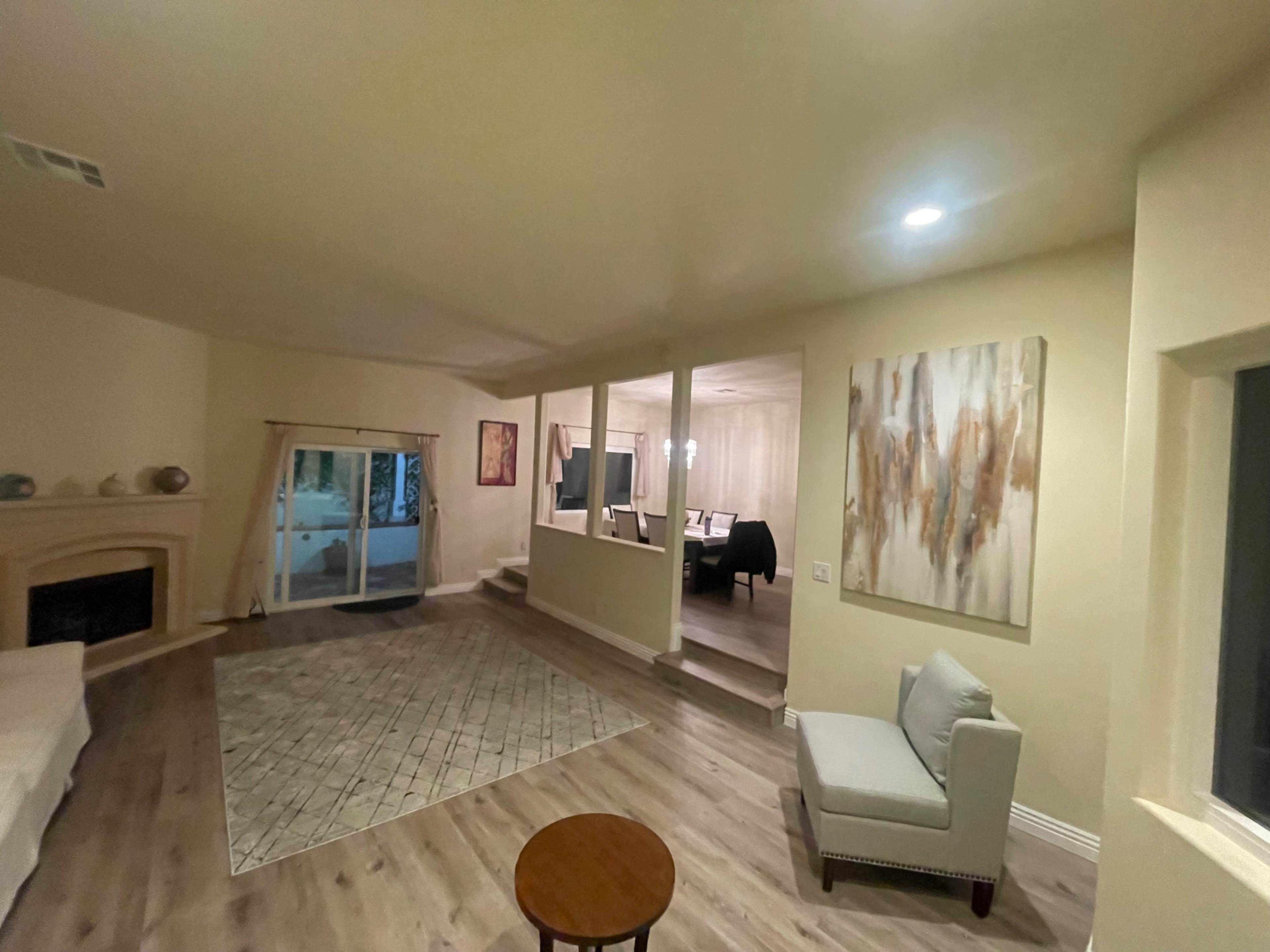 A spacious living area with a fireplace, a sliding door to an outside patio, and a dining area visible in the background.
