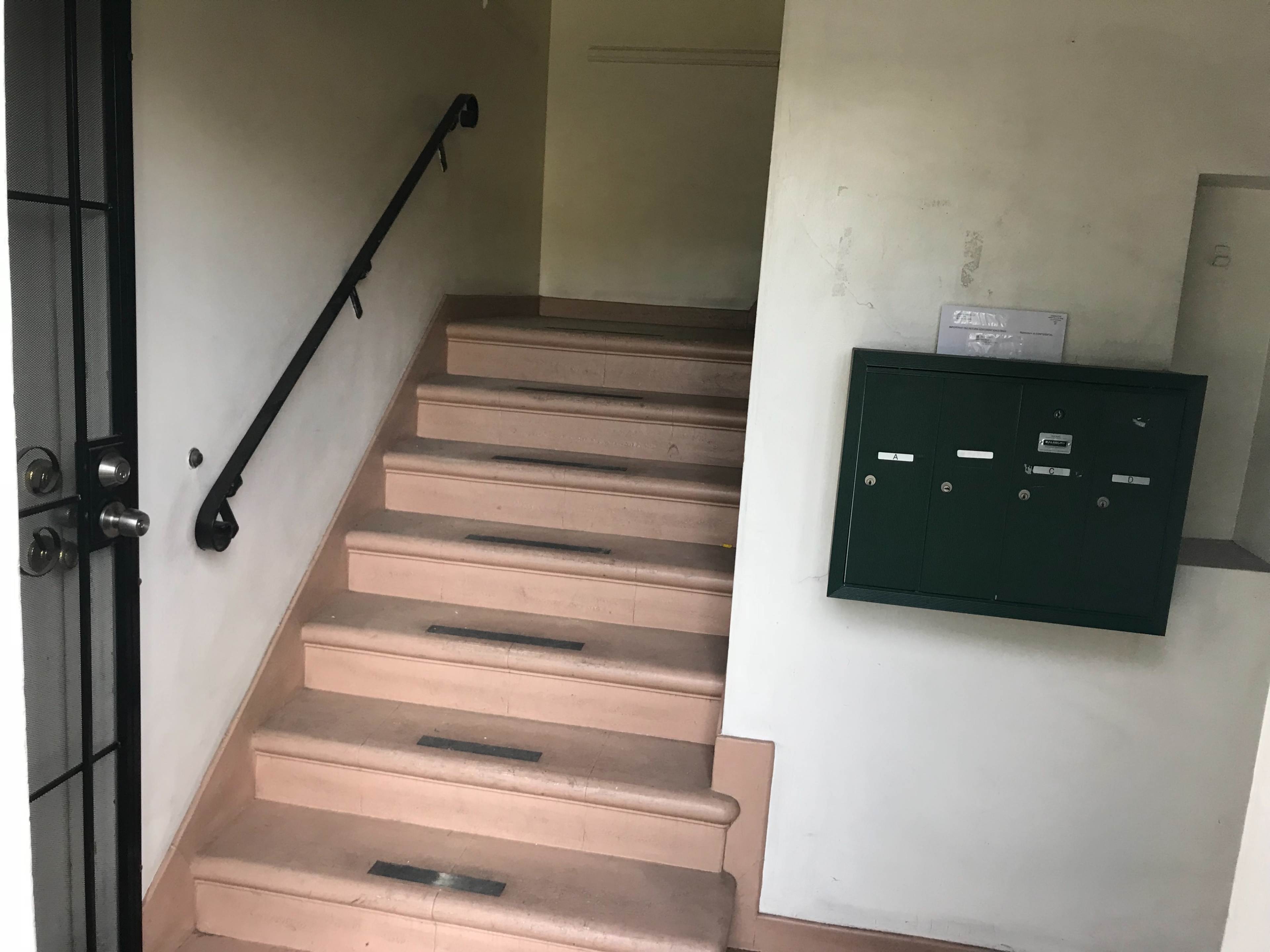 The image shows a staircase leading to an upper level, with a mailboxes mounted on the wall beside it.