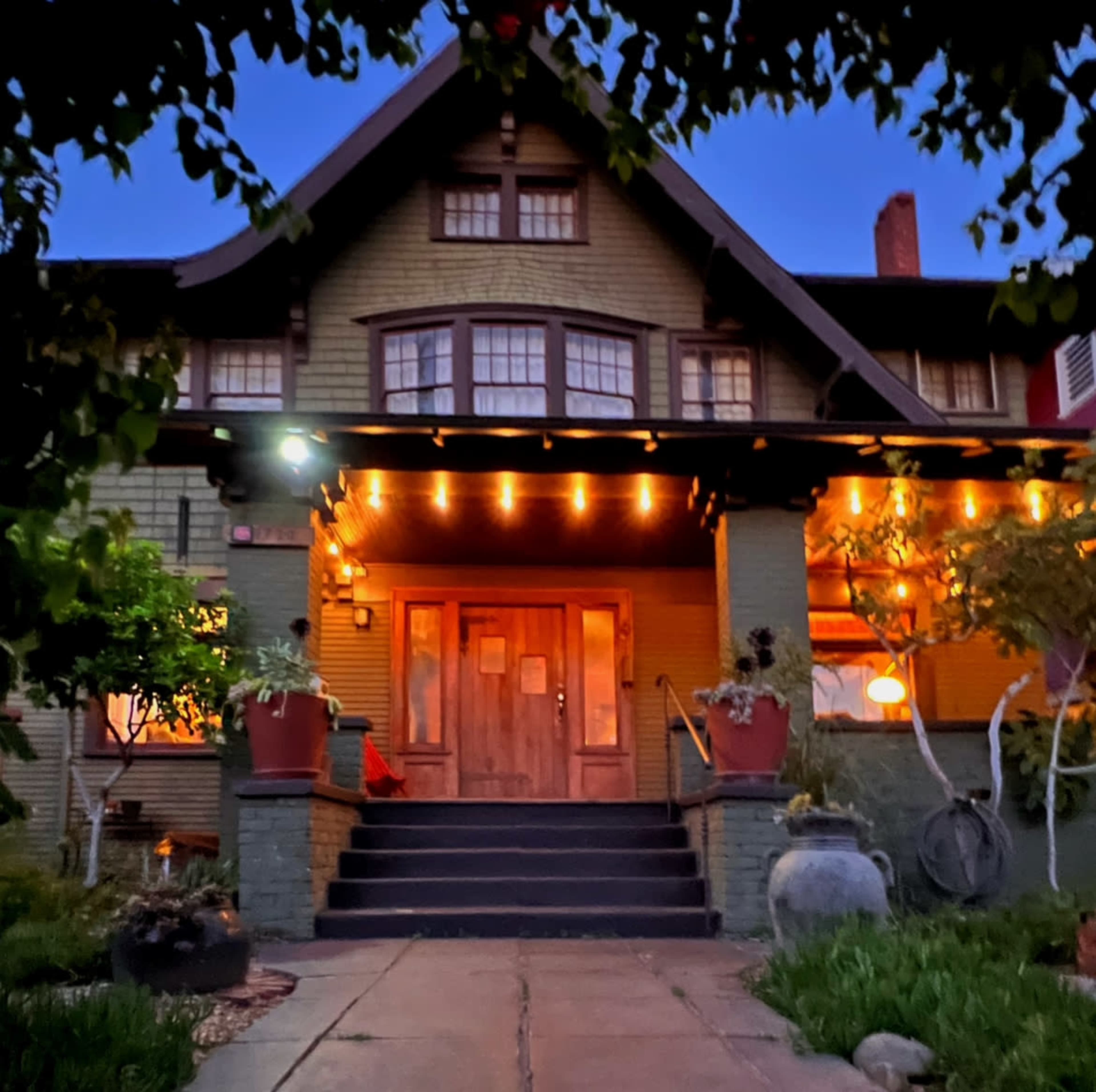 A two-story green house with a sloped roof, illuminated porch lights, and a well-maintained front yard.
