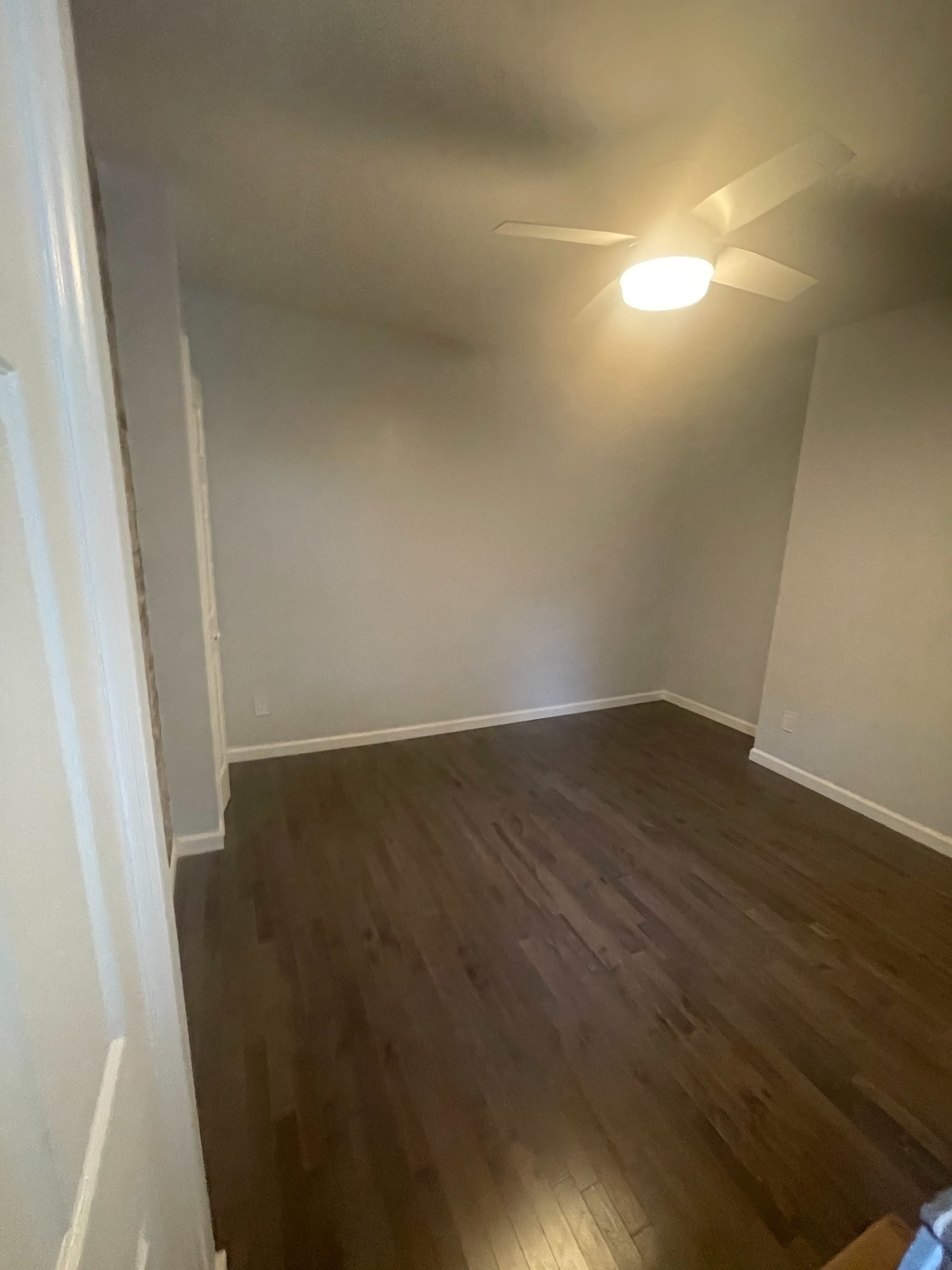 A vacant room with a ceiling fan and hardwood flooring.