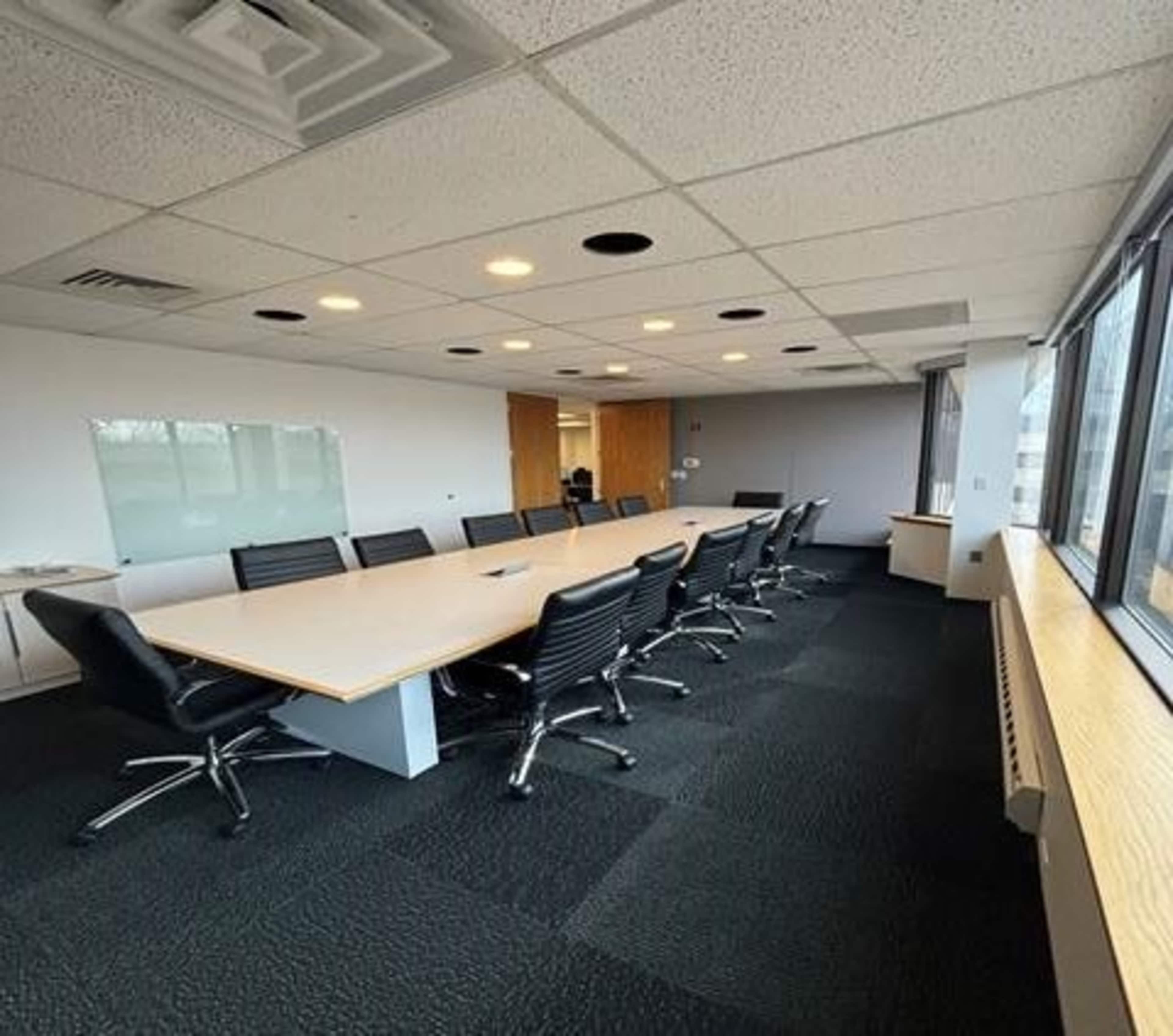 A conference room features a long table surrounded by black swivel chairs, with large windows providing natural light.