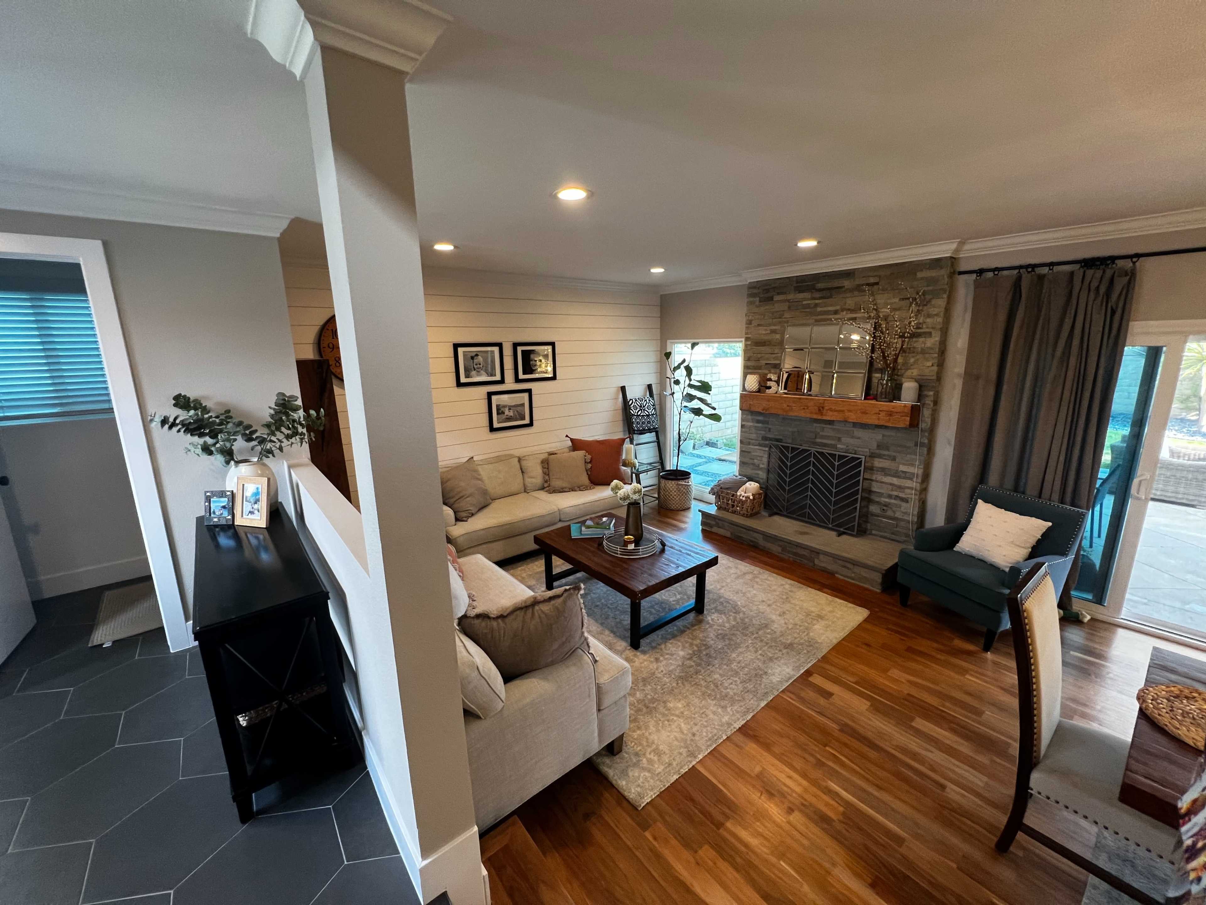 The image shows a cozy living room featuring a stone fireplace, a comfortable sofa, and a combination of wooden and stone decor on the walls and furnishings.