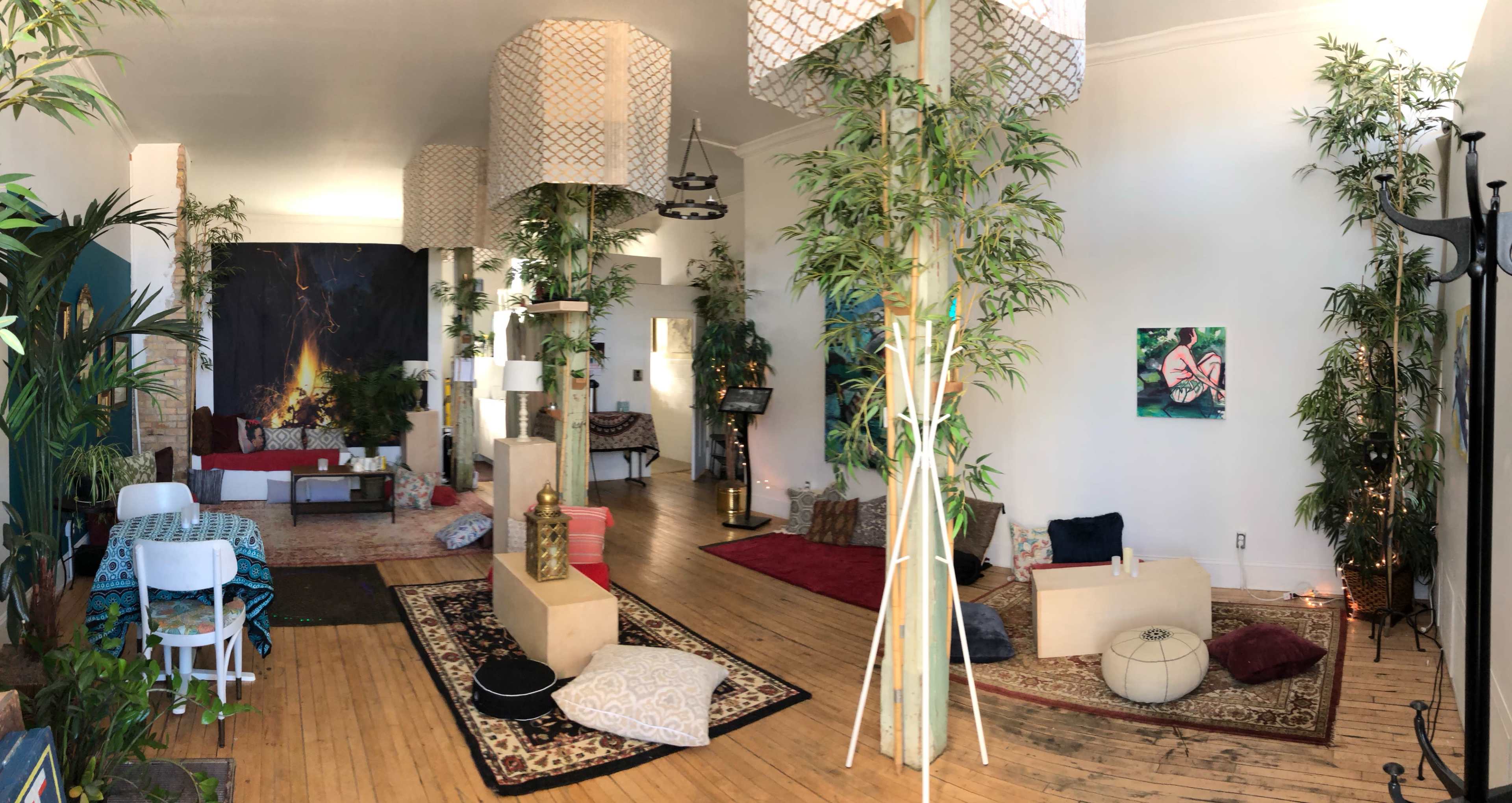 A spacious room filled with plants, decorative lamps, various seating arrangements, and artworks on the walls.