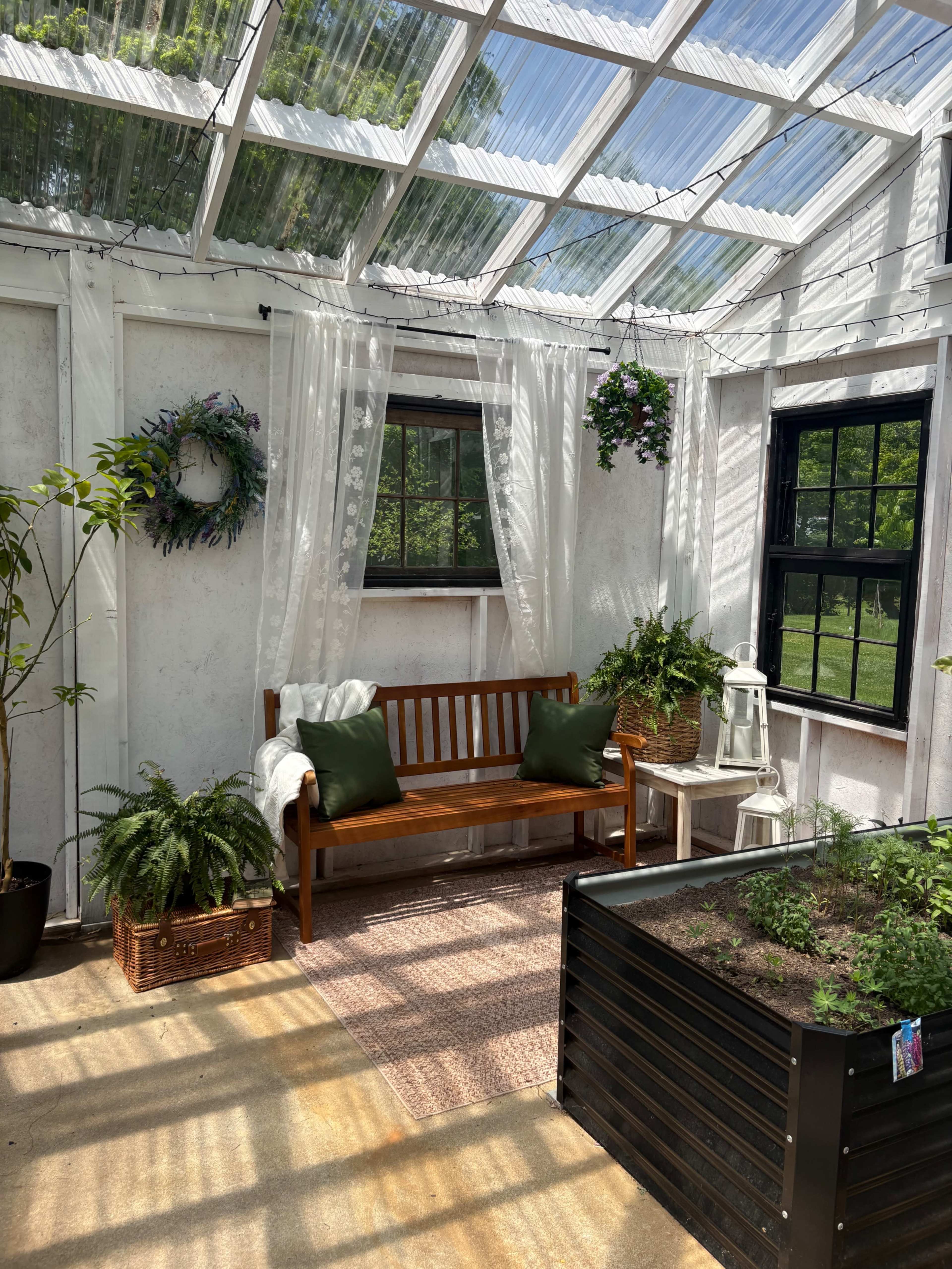 The image shows a bright indoor greenhouse with a wooden bench, potted plants, and a garden bed.