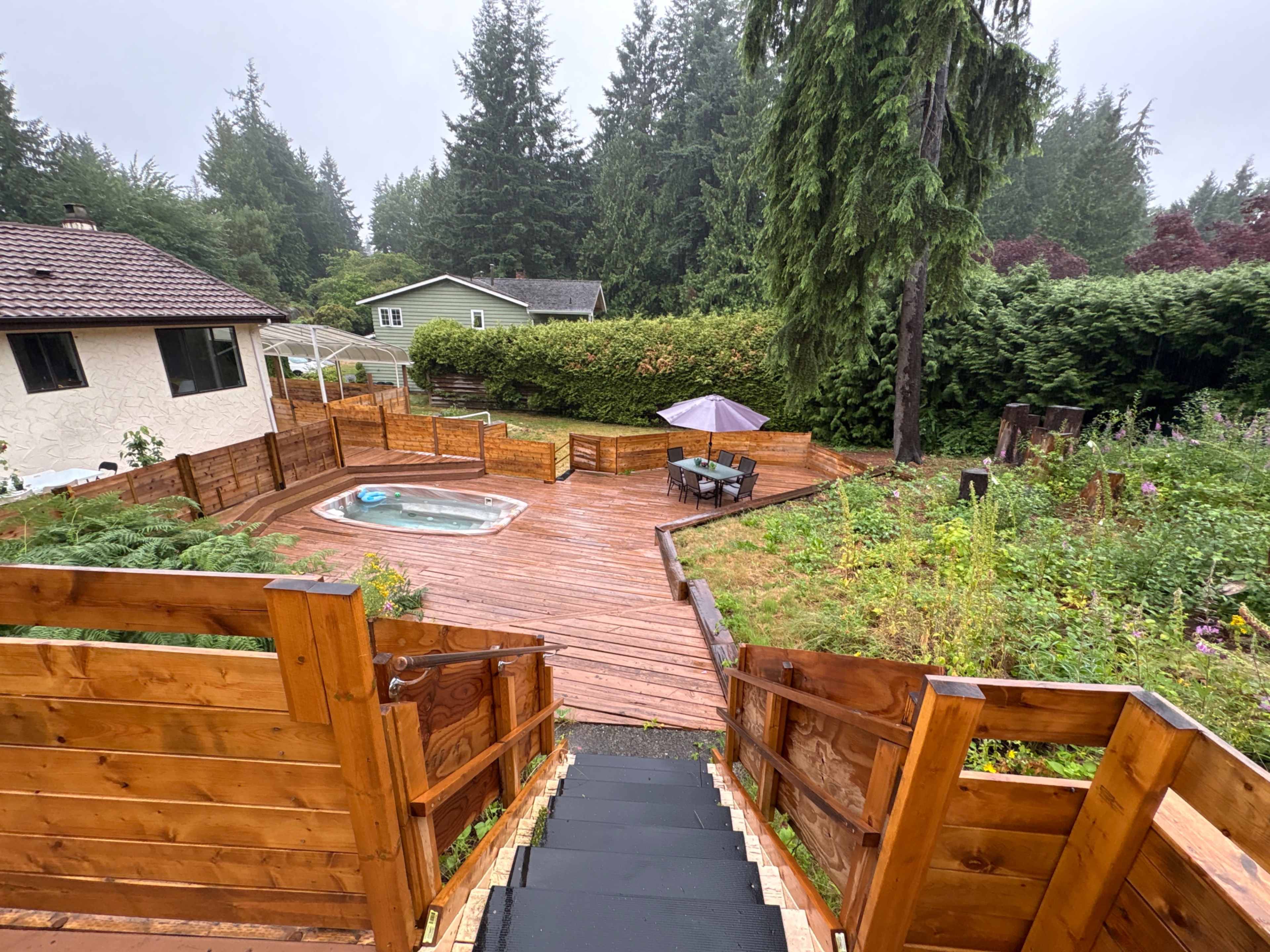 A wooden stairway leads down to a backyard with a swimming pool, surrounded by a wooden fence and various trees.