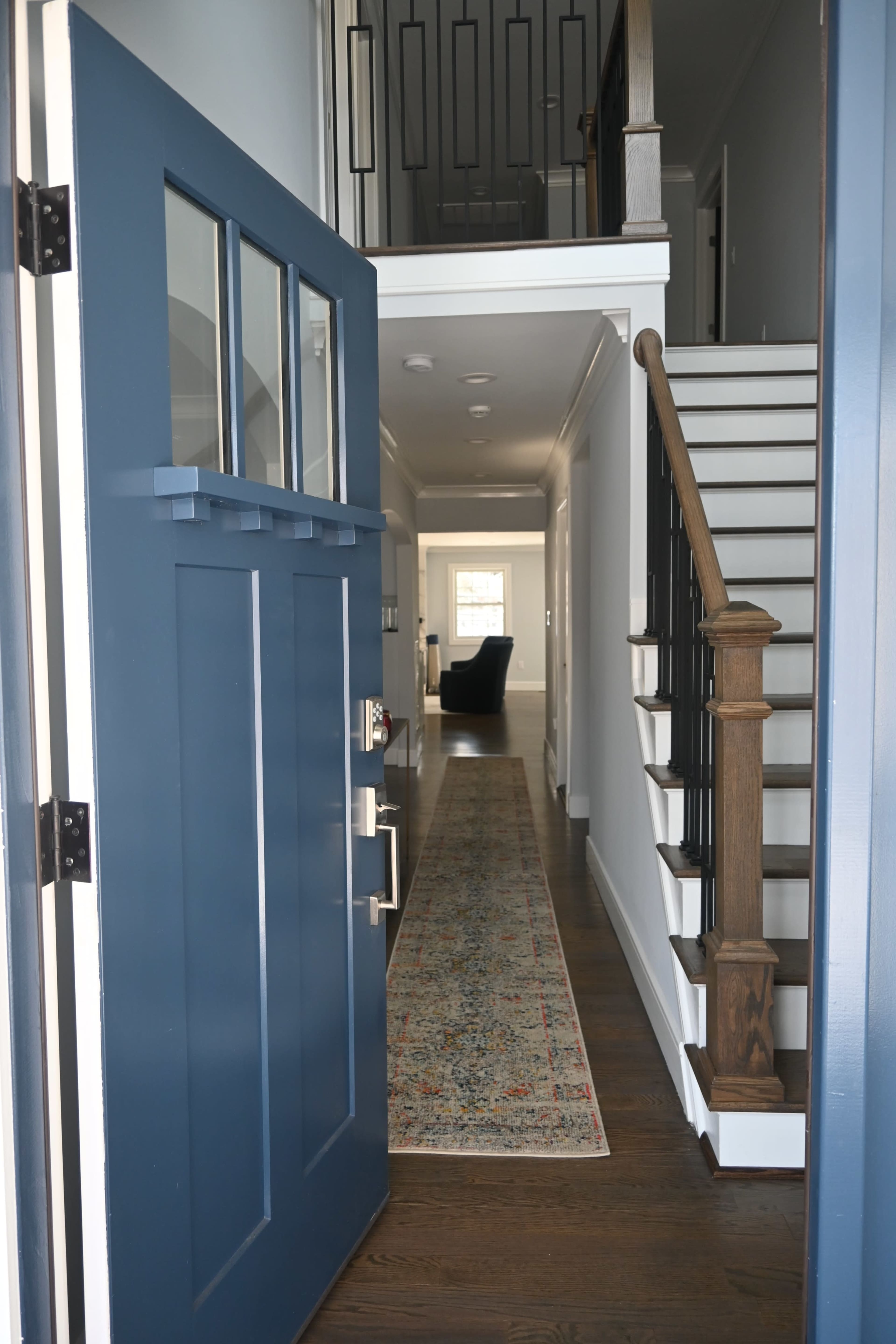 A blue front door opens to a hallway with stairs leading to an upper level and a patterned runner rug on the floor.