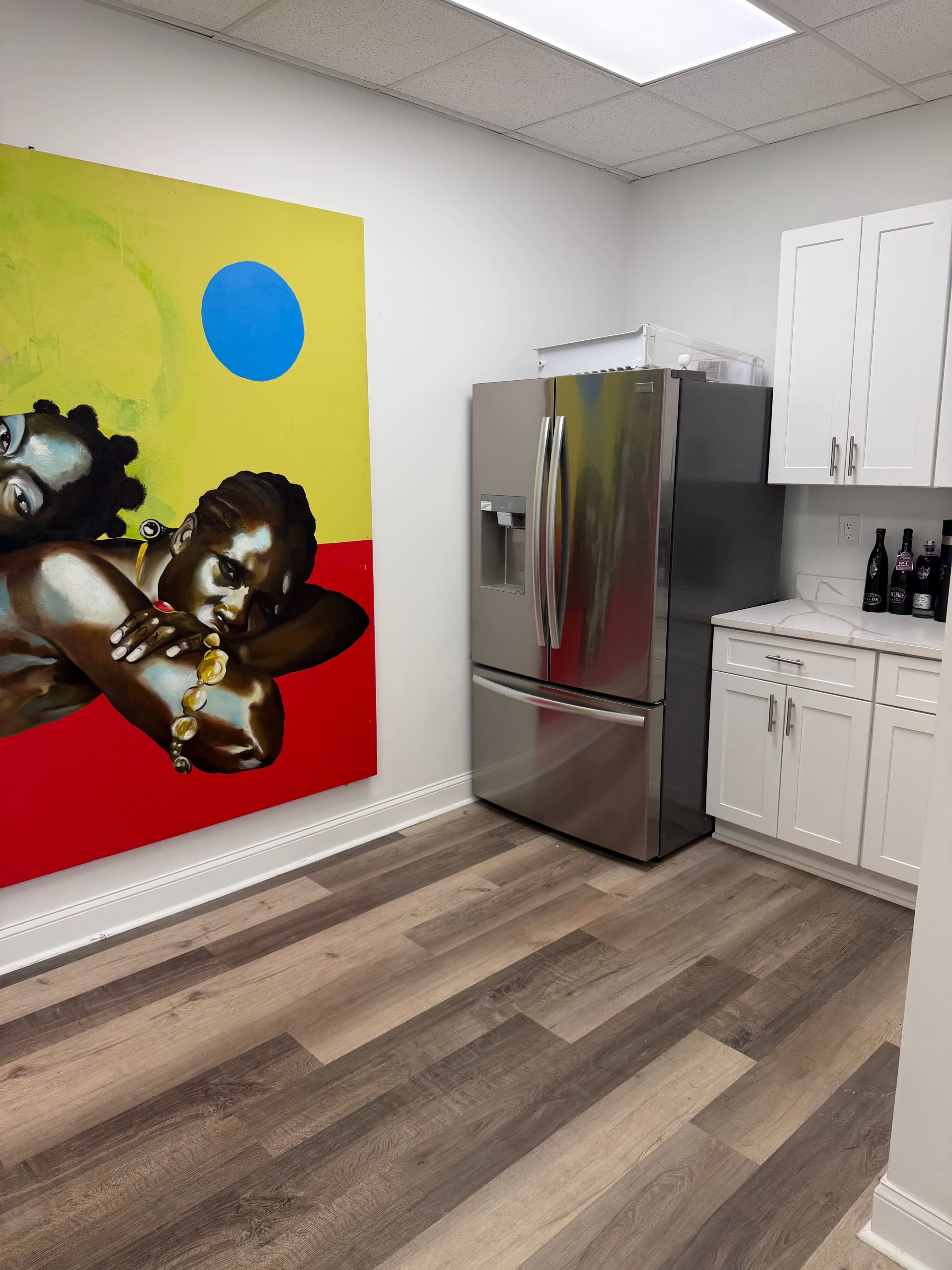 The image shows a modern kitchen featuring a stainless steel refrigerator and a colorful mural on the wall.