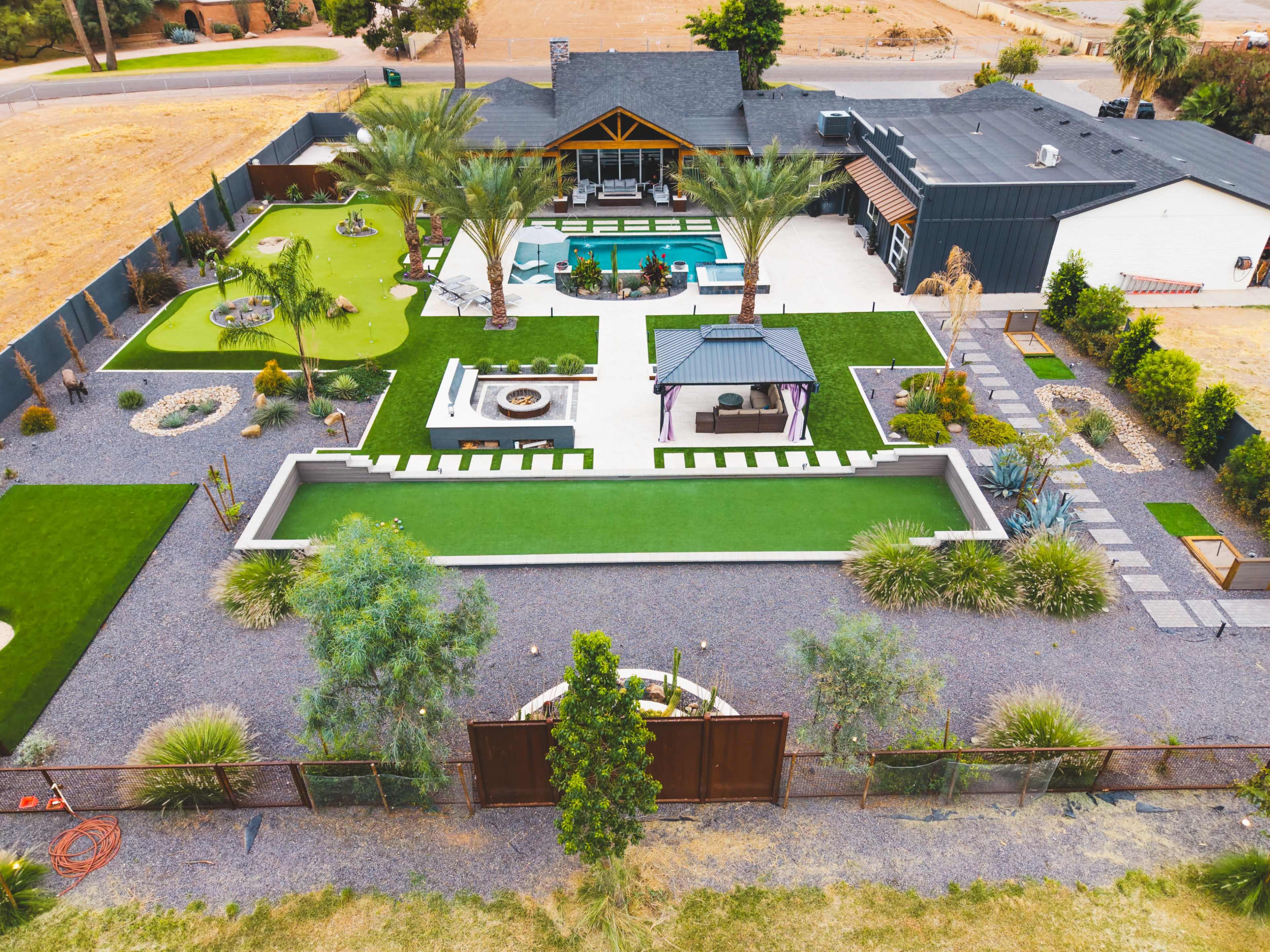 The image shows an expansive outdoor space featuring a swimming pool, landscaped green areas, a gazebo, and various seating arrangements.