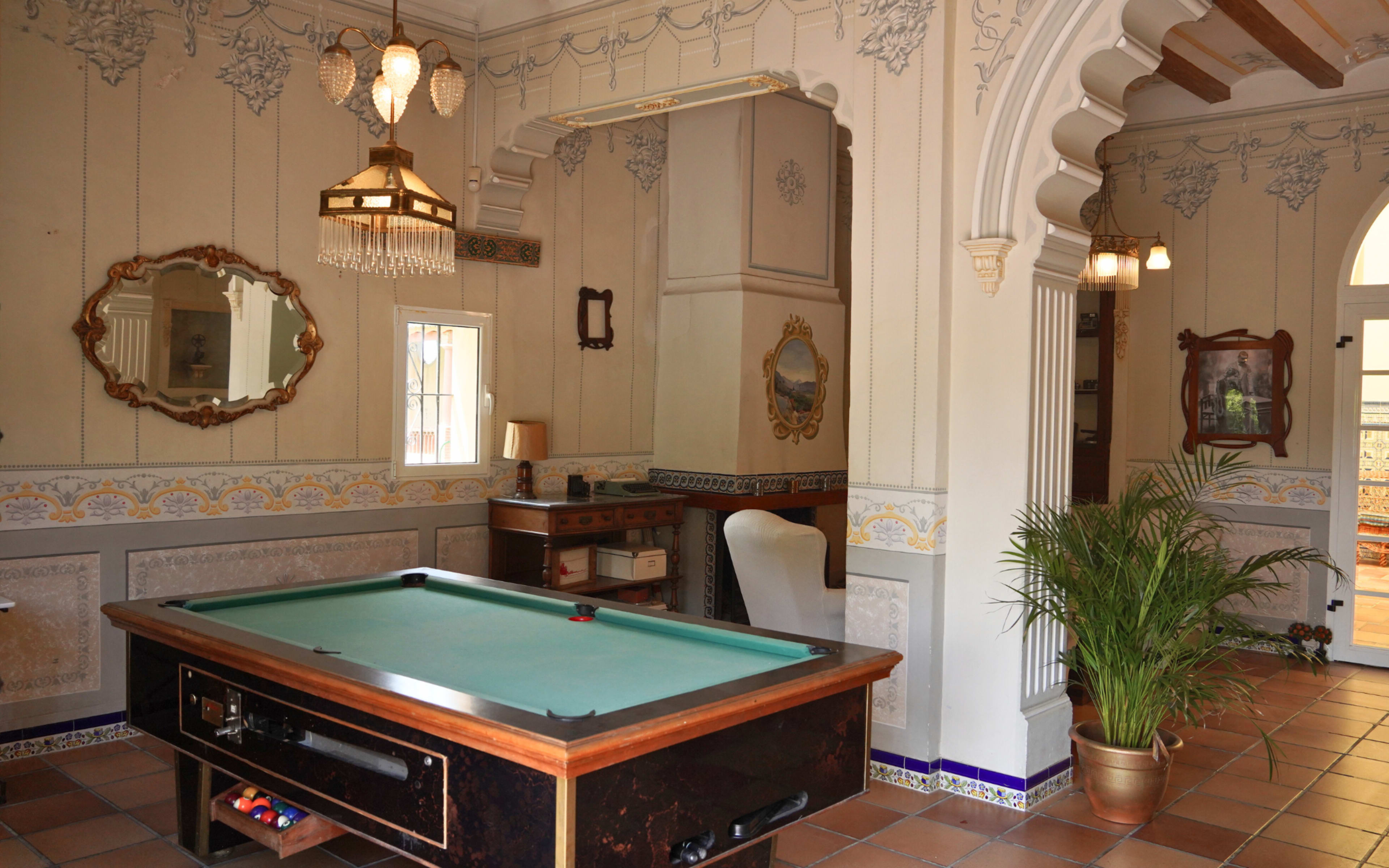 The image shows a well-decorated room featuring a pool table, elegant wall mirrors, and classical architectural details.