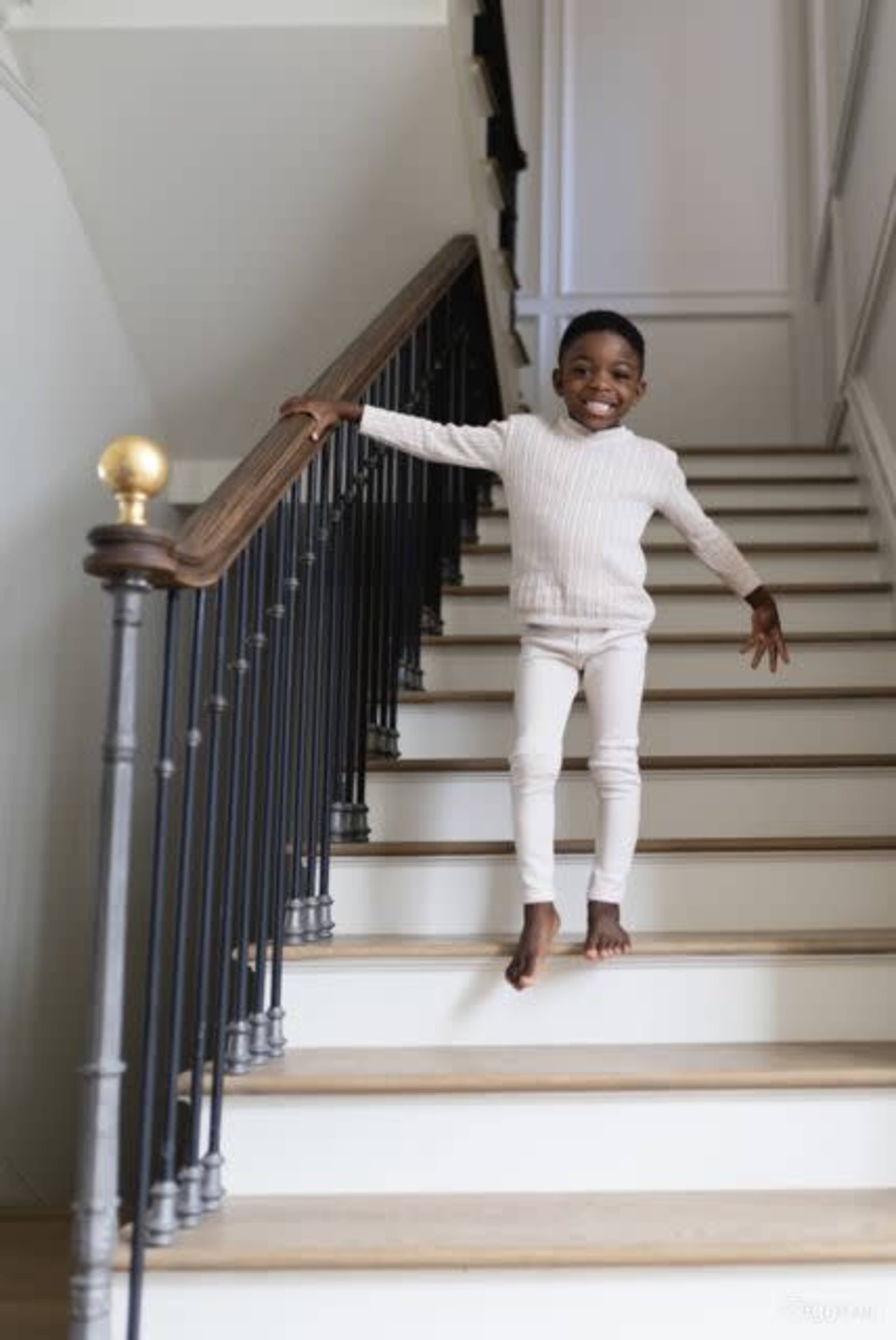 A child is playfully balancing on the railing of a staircase in a bright, modern home.