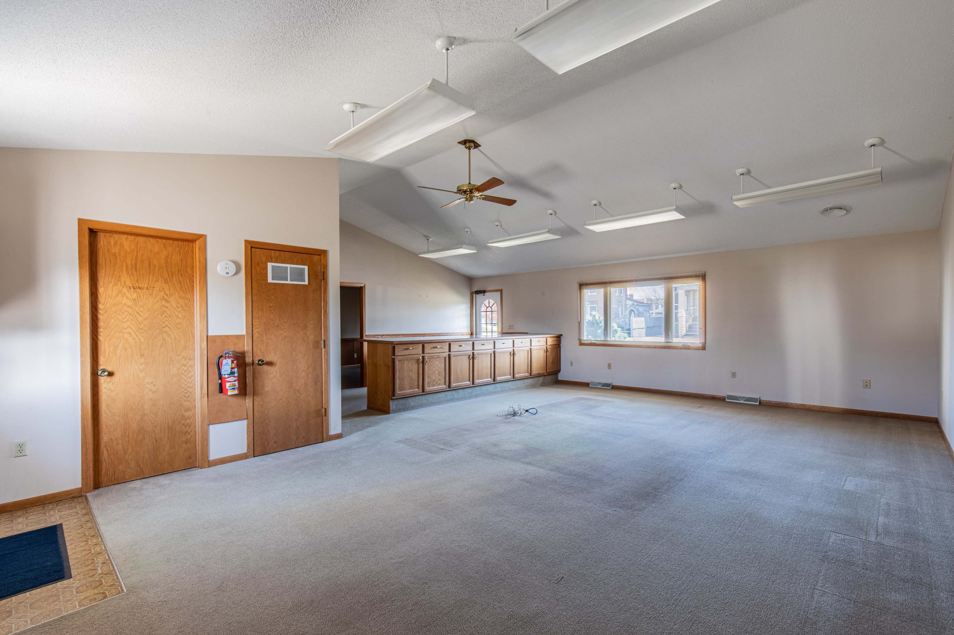 A spacious room with beige carpet, a ceiling fan, and two wooden doors.