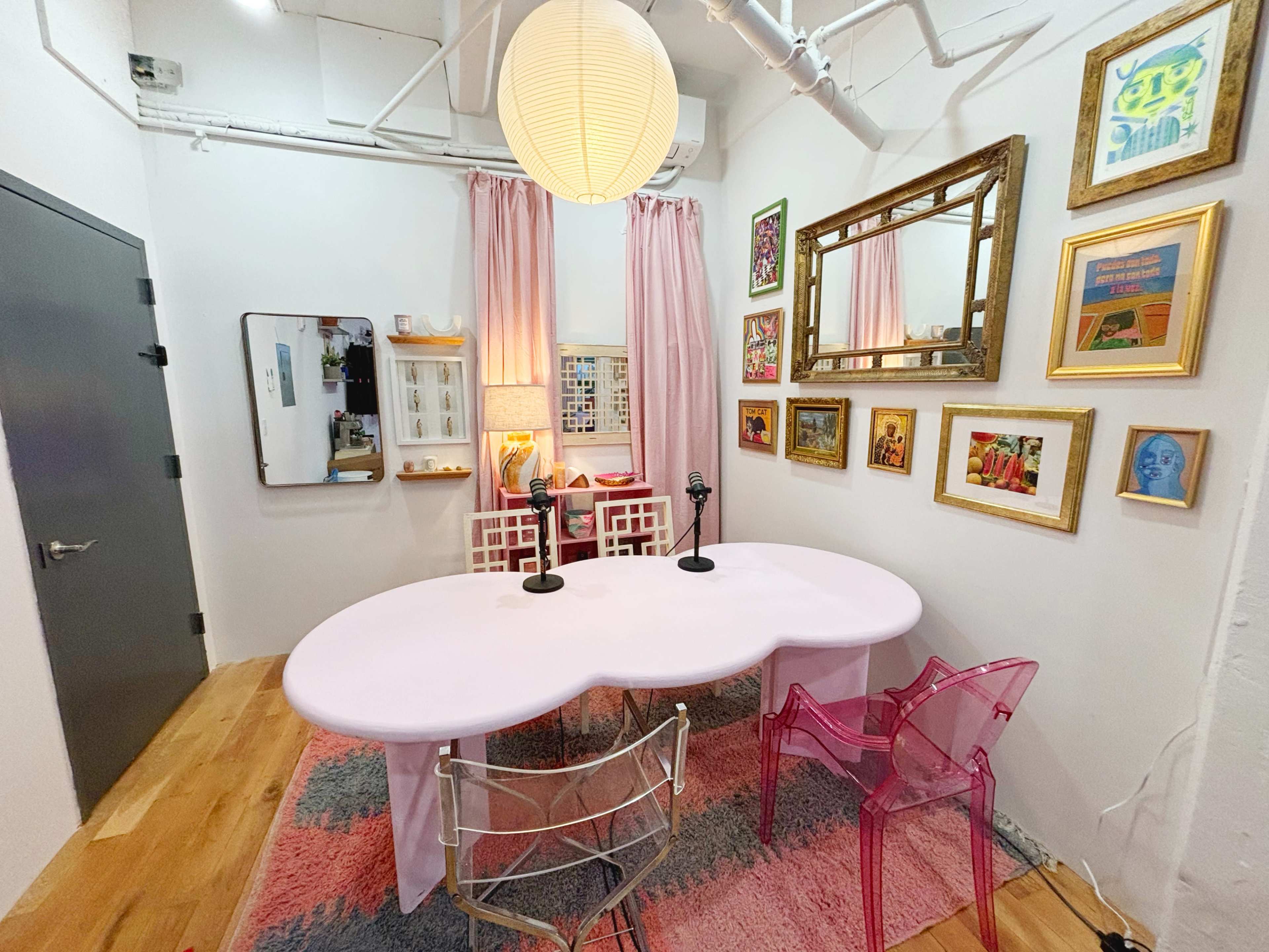 The image shows a brightly colored room featuring a cloud-shaped pink table, two microphones, and various framed artworks on the walls.