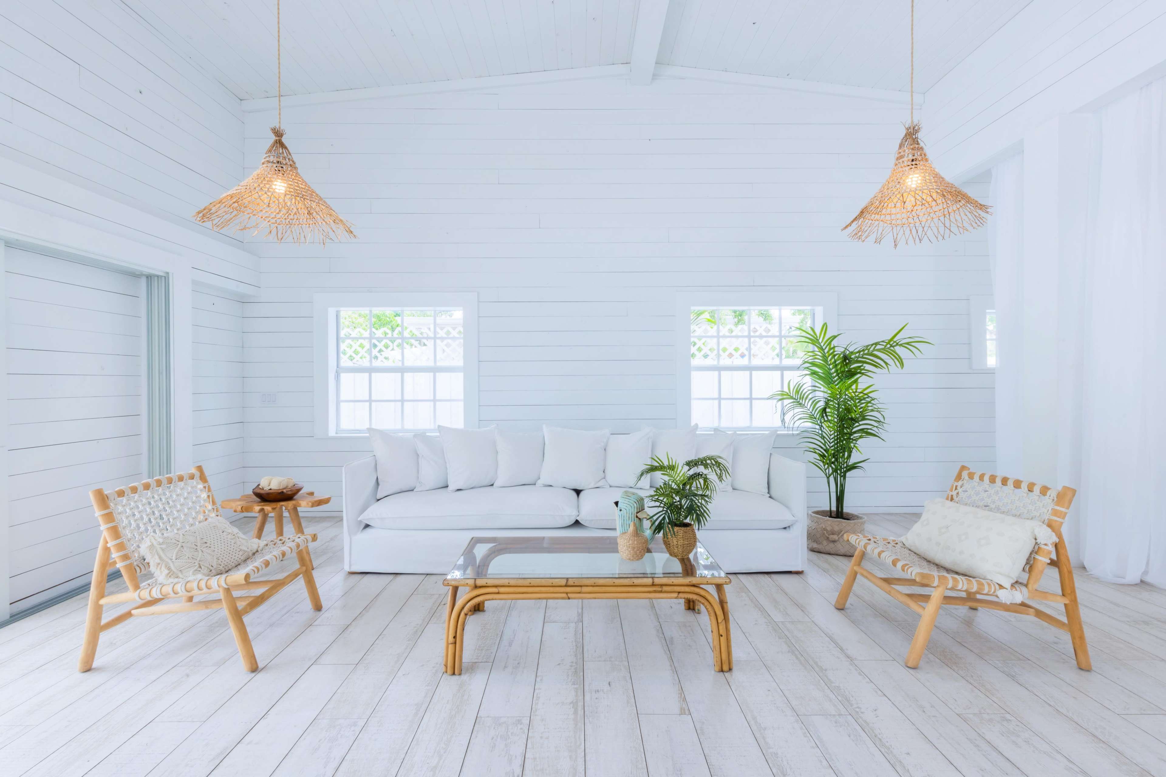 The scene features a minimalist living room with white walls, a white sofa, bamboo furniture, and natural light streaming through windows.