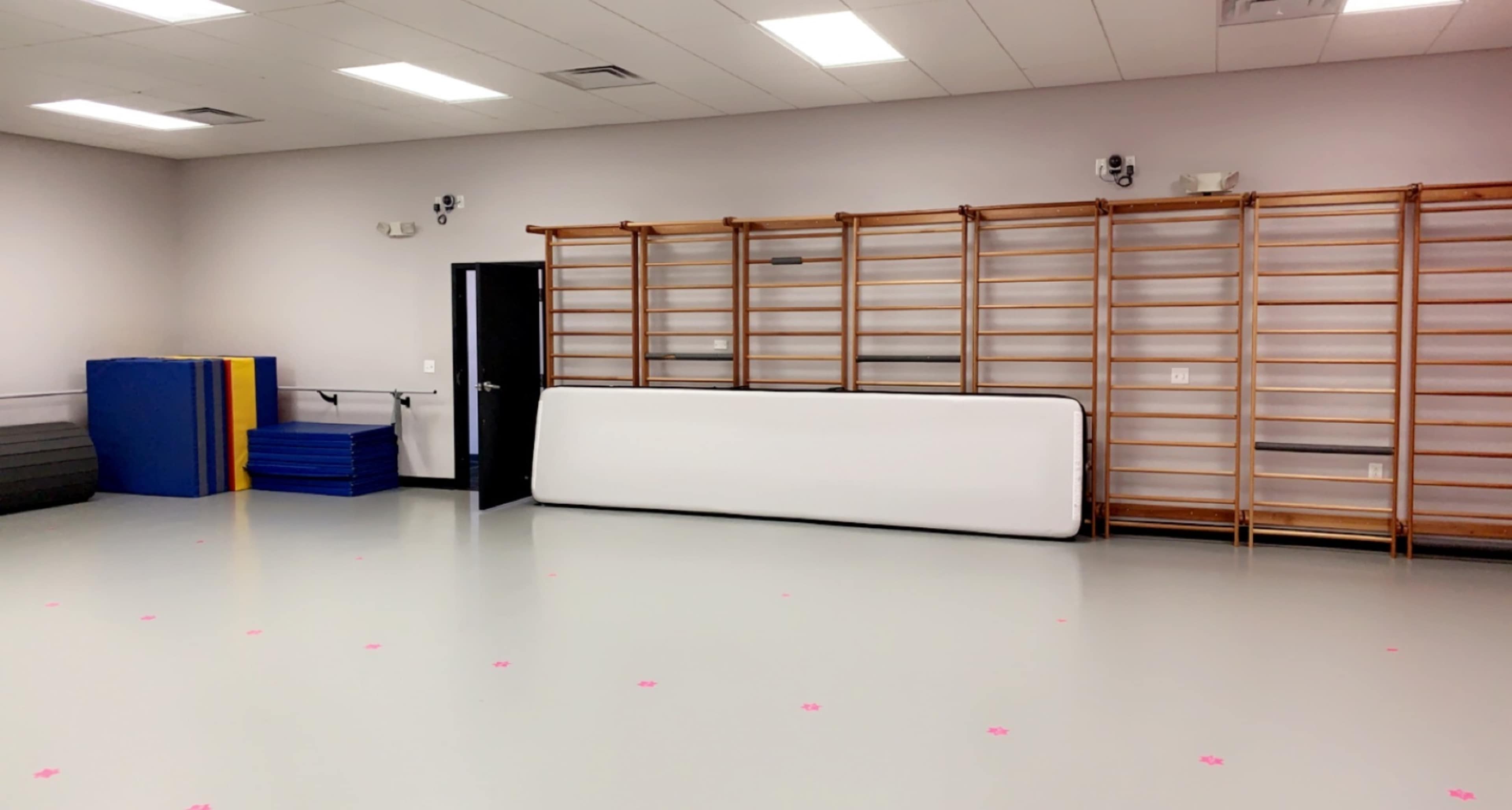 A spacious exercise or gym area with padded mats stacked against the wall and a series of wooden wall bars installed on another wall.