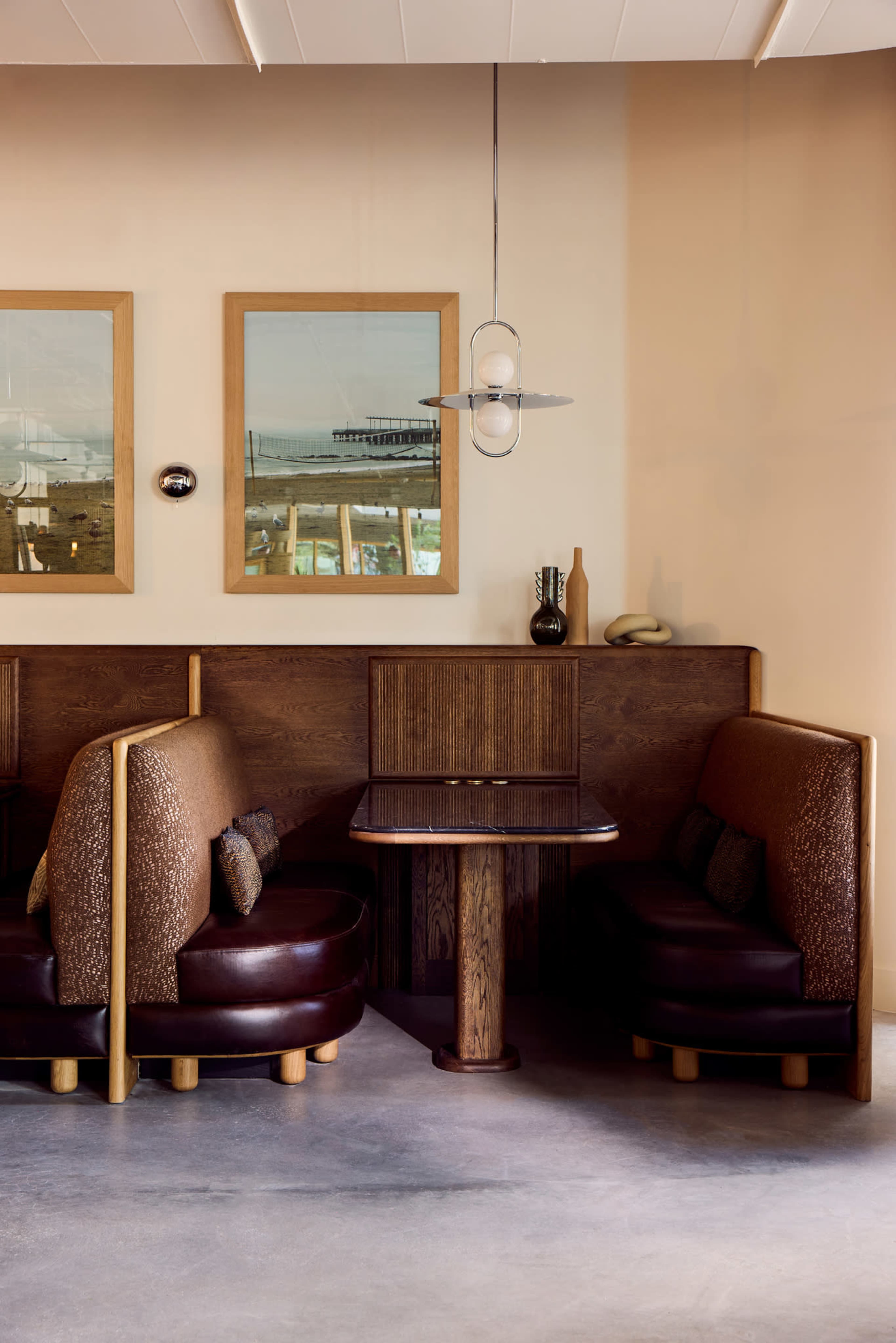 The image shows a cozy restaurant corner featuring dark wooden booths, a round table, and framed pictures on the walls.