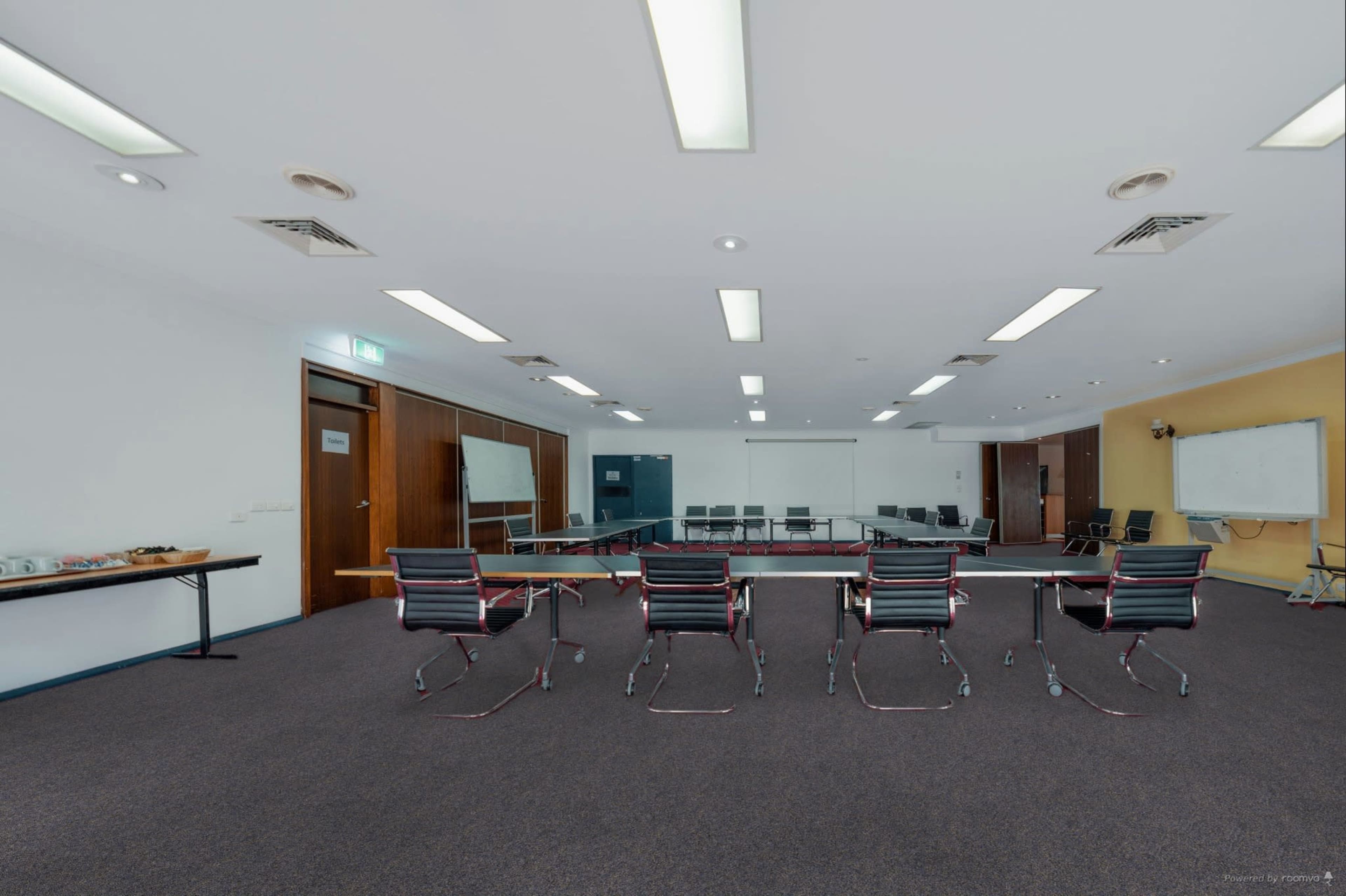 A spacious conference room features a long table with rolling chairs, whiteboard, and multiple seating areas.