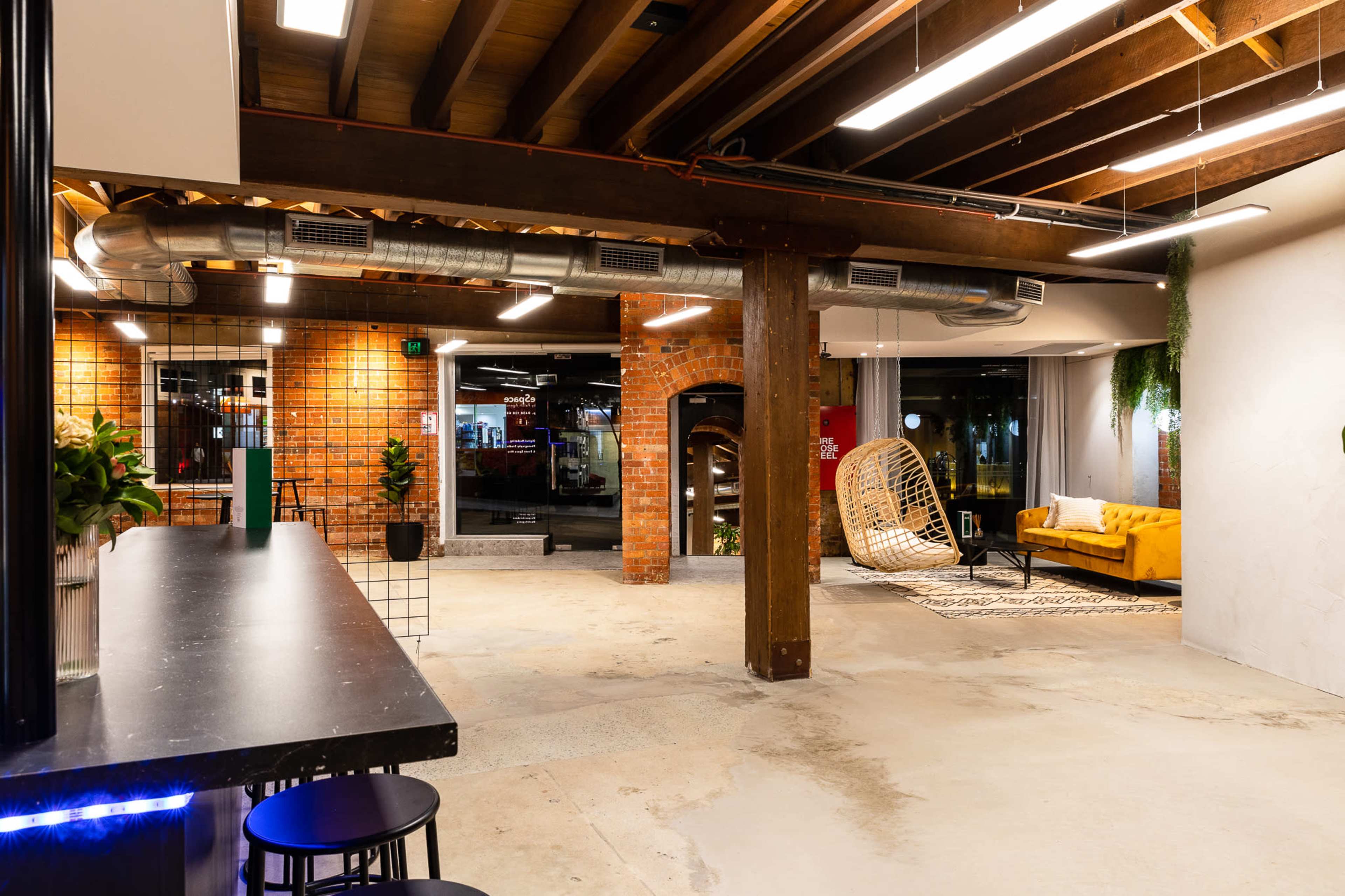 A spacious, modern interior featuring exposed wooden beams, a seating area with a yellow couch, and a bar counter with black stools.