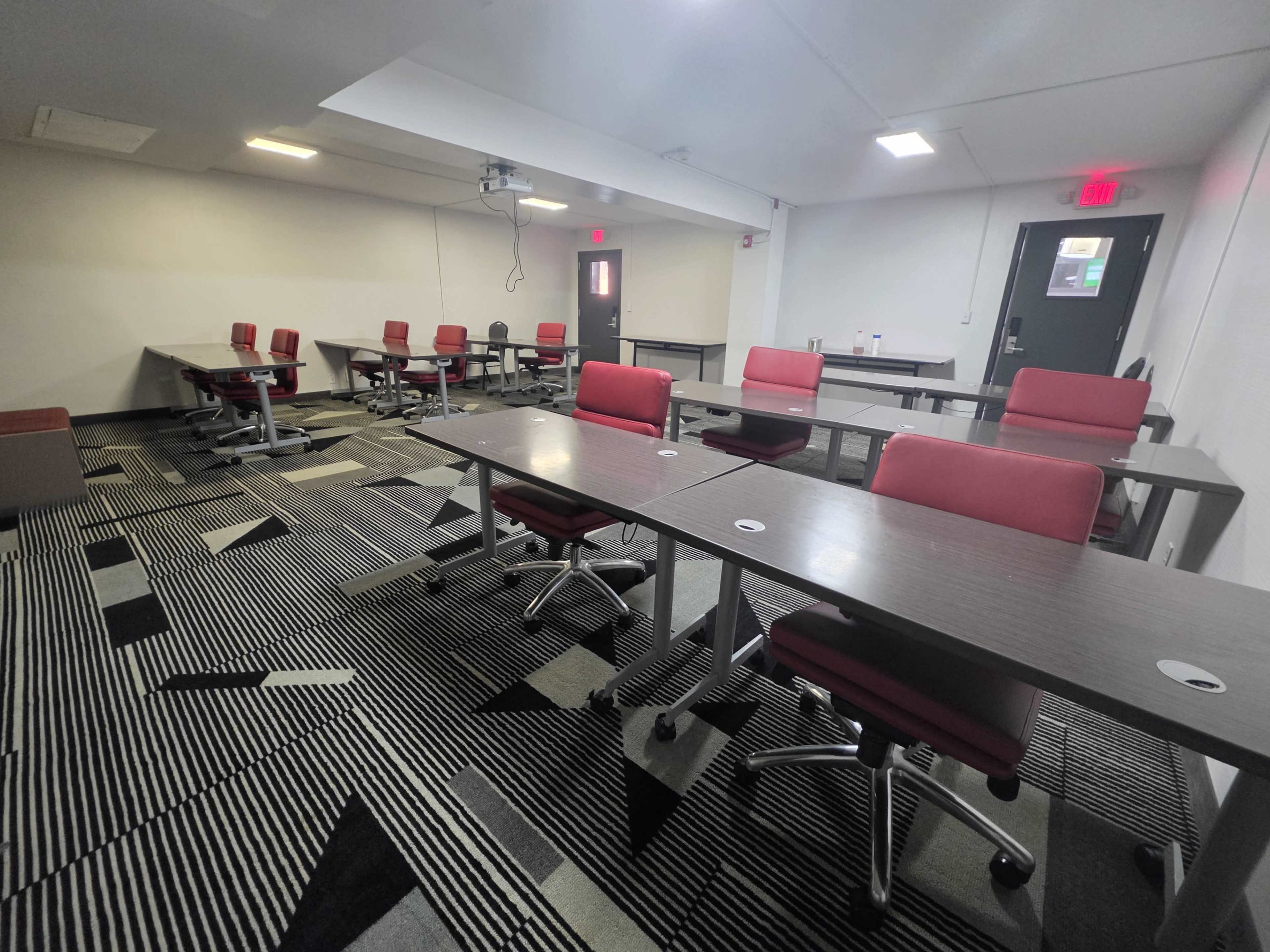 The image shows a modern meeting room with several tables and red chairs arranged in a spacious layout, featuring carpet with a geometric pattern.