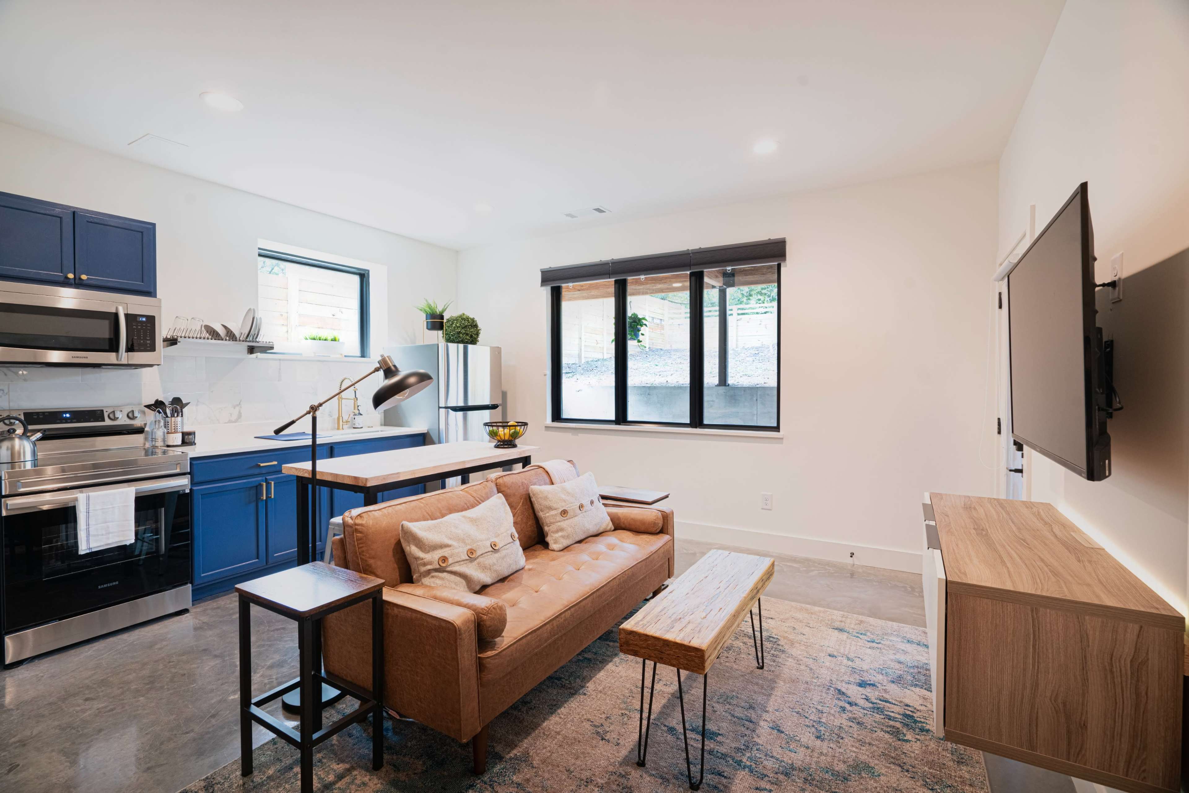 A modern living area featuring a brown sofa, wooden coffee table, and a kitchen with blue cabinets and stainless steel appliances.