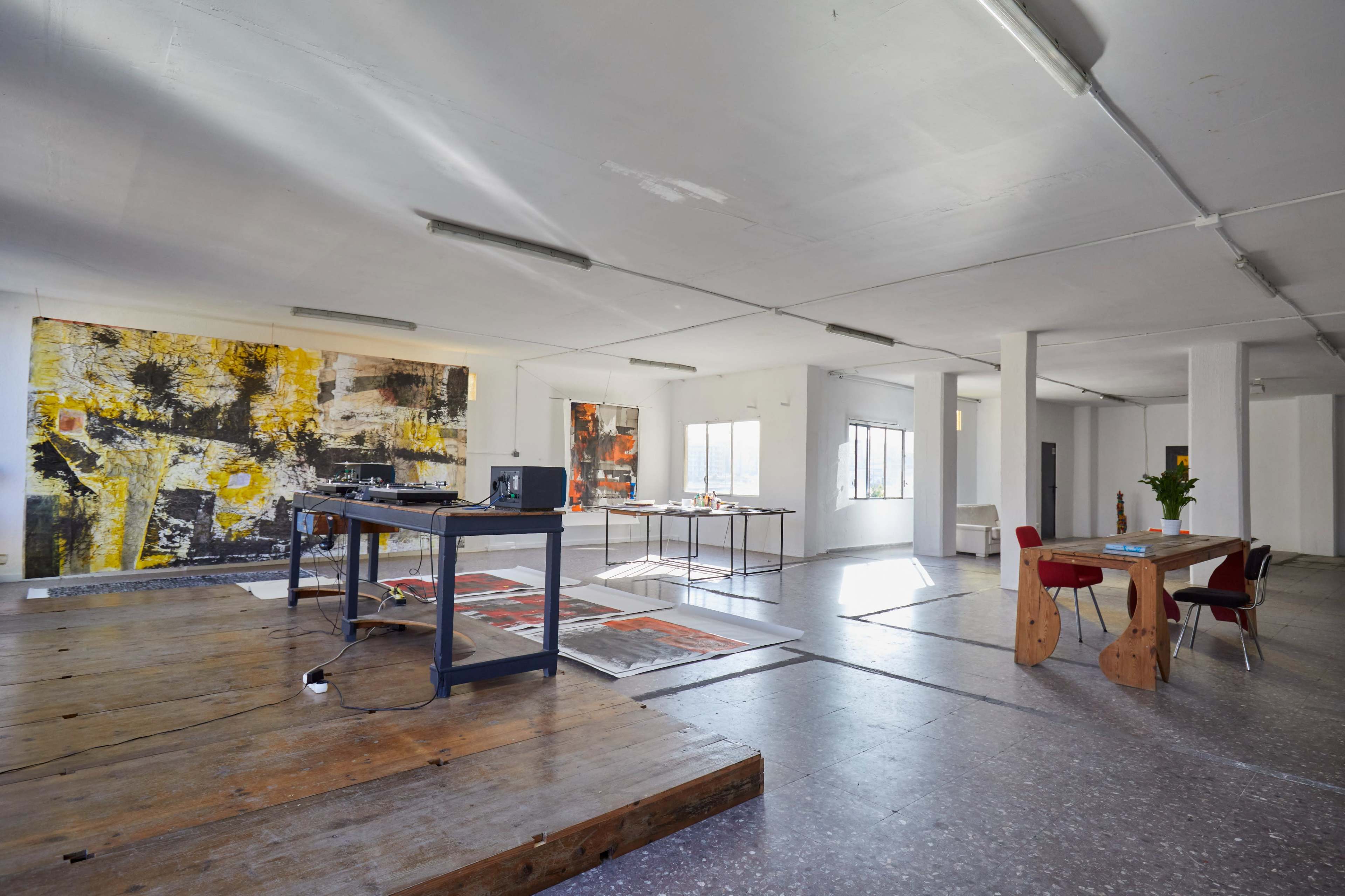 An open, spacious studio area featuring large abstract paintings on the walls, a wooden table with a projector, and modern furniture including a dining table and chairs.